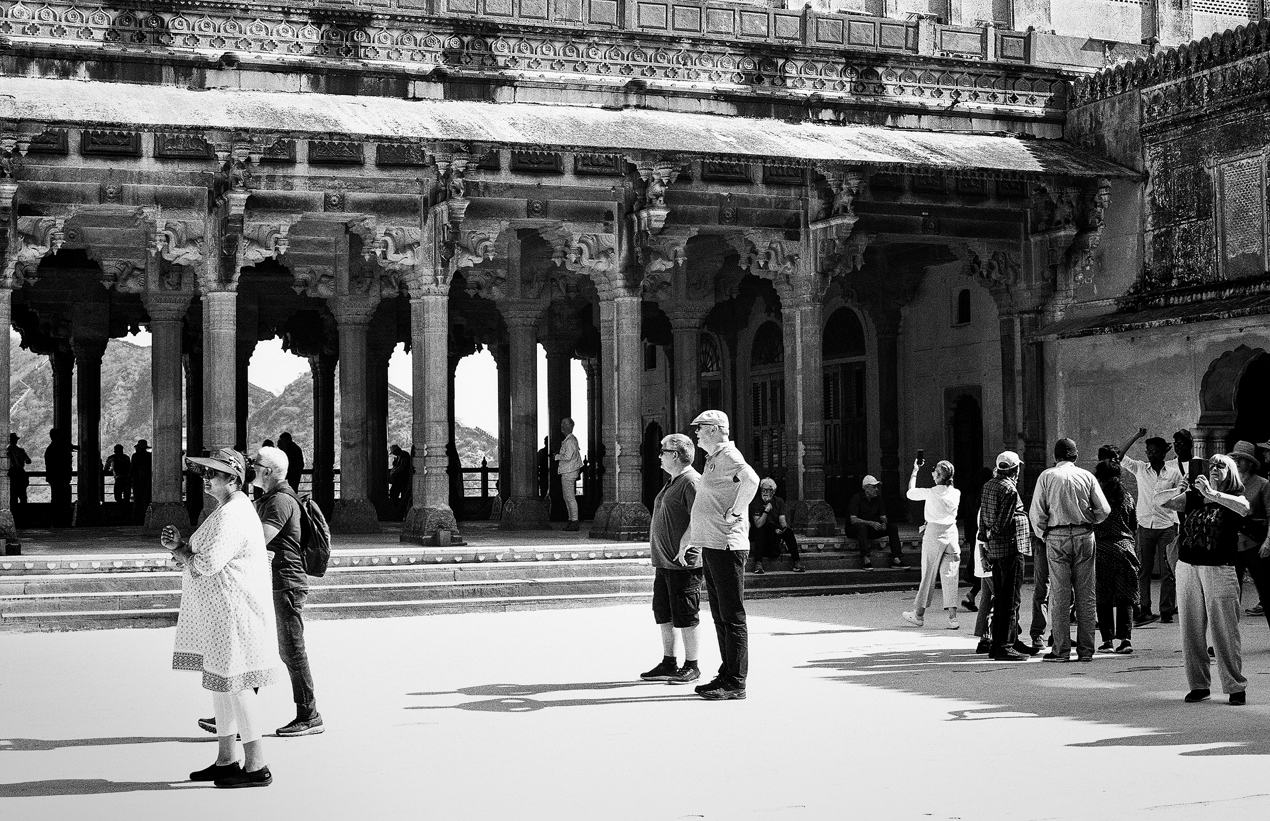 Black and white palace courtyard with ornate columns visitors in light clothing mountain landscape
