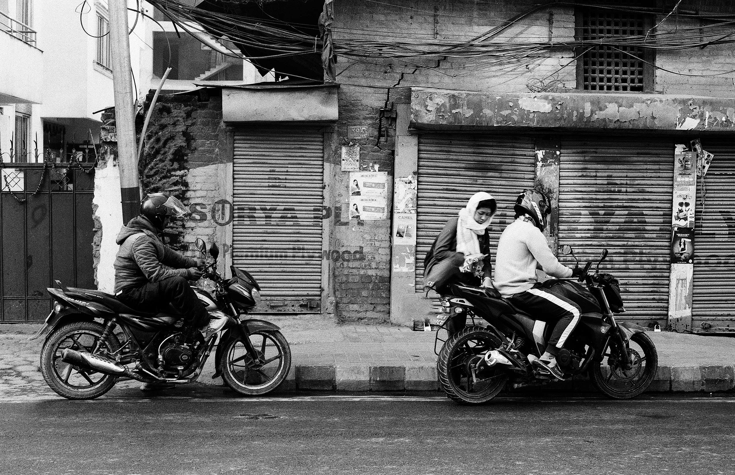 Street scene with two people on motorcycles in front of shuttered storefronts
