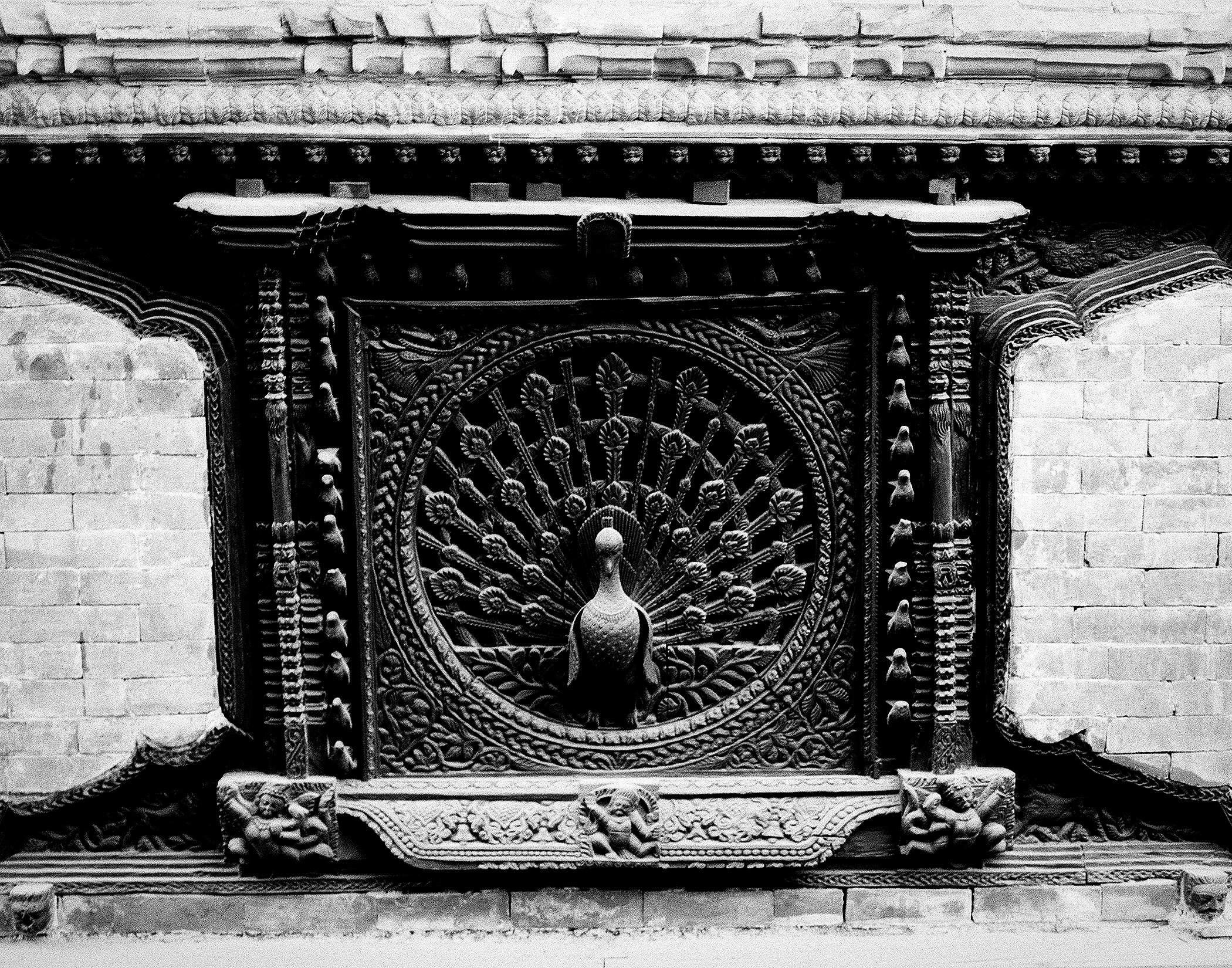 Ornate carved stone peacock relief panel centered on decorative temple wall