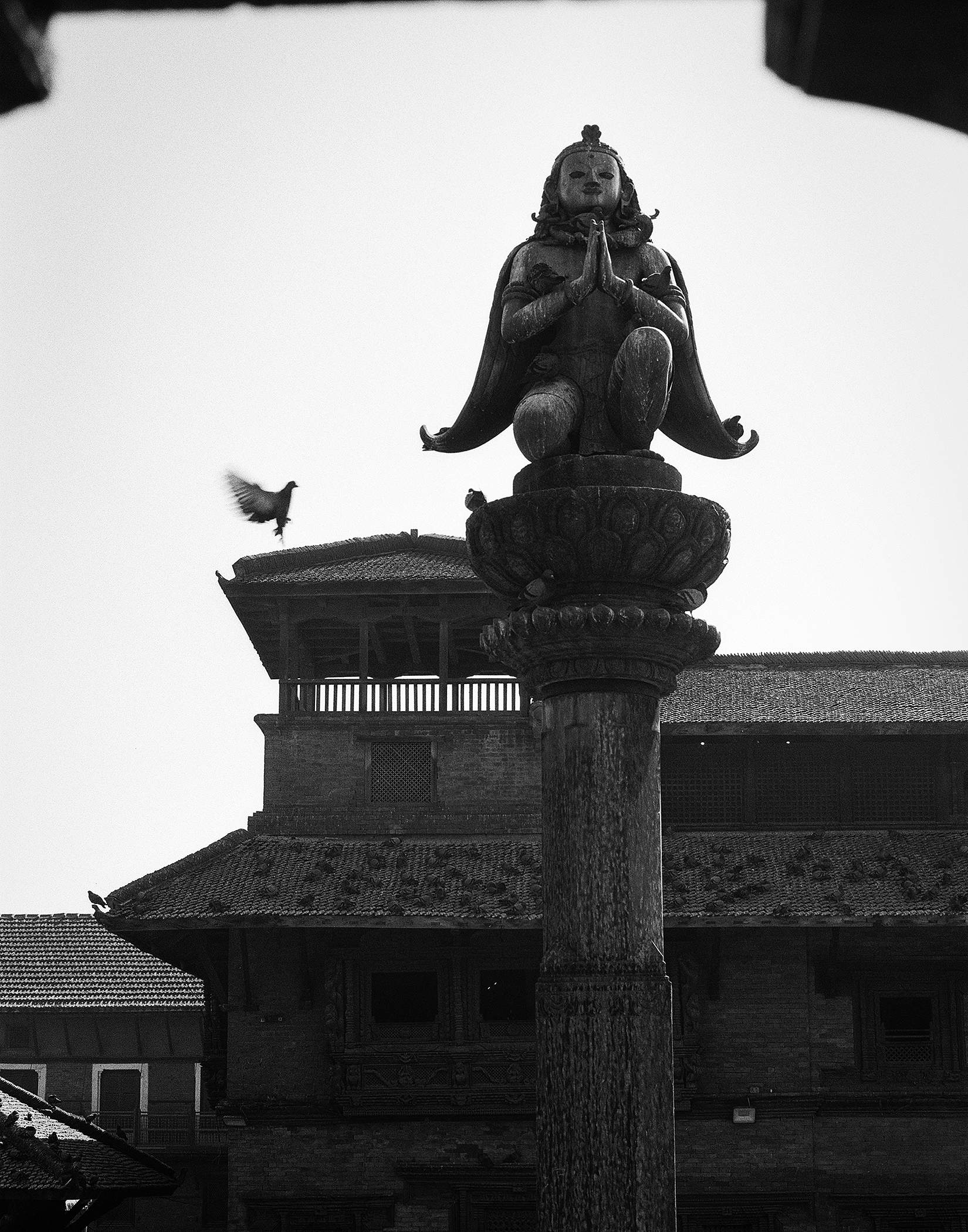 Stone sculpture of goddess figure in meditation pose on ornamental column with architectural details