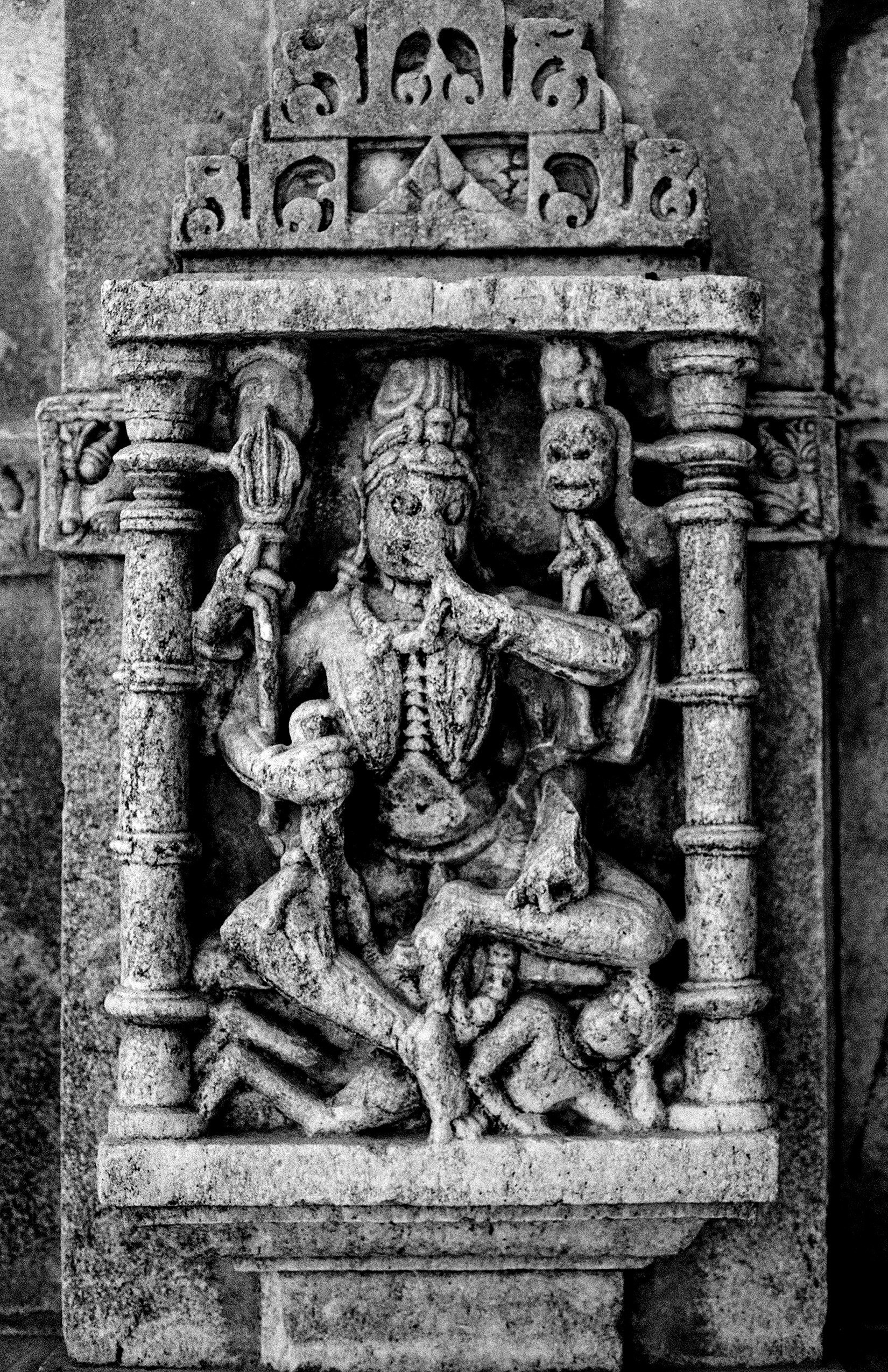 Black and white detailed Hindu temple stone carving relief showing seated deity with ornate pillars