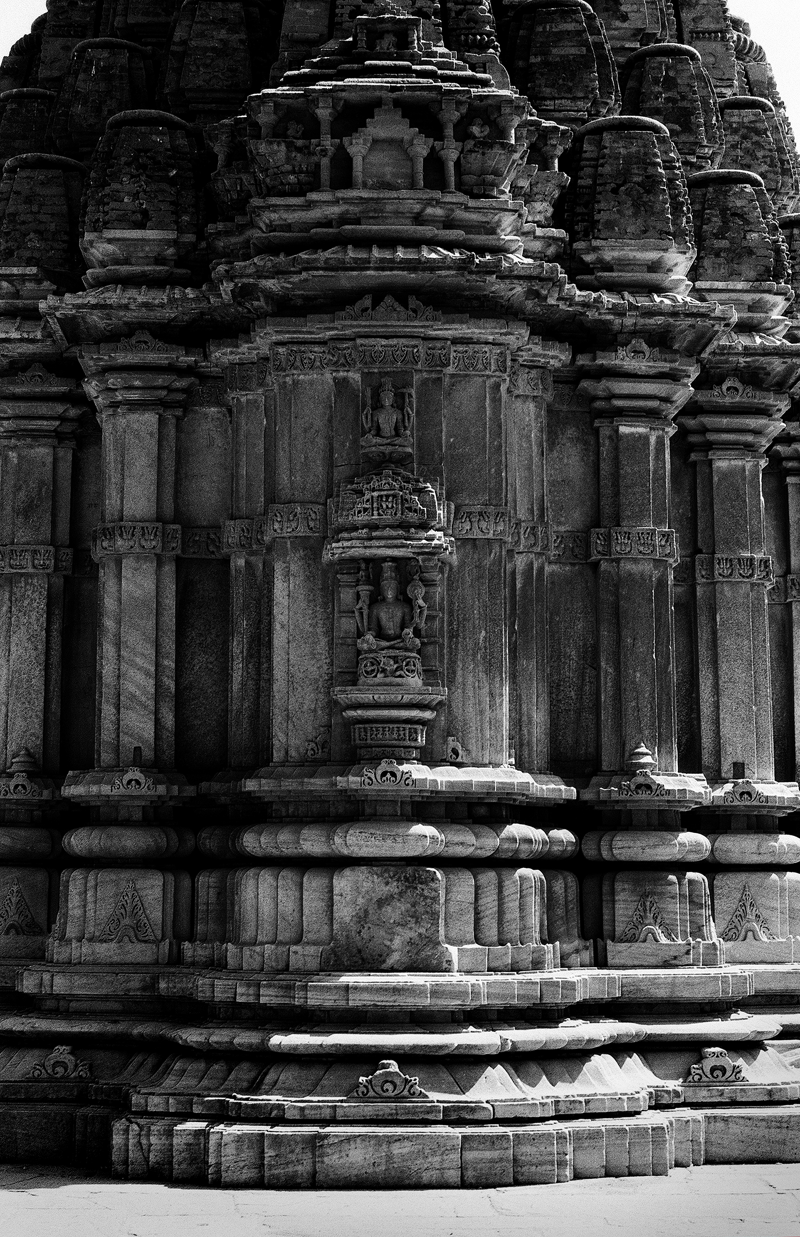 Black and white temple exterior with detailed carved columns niches with deity figures stepped base
