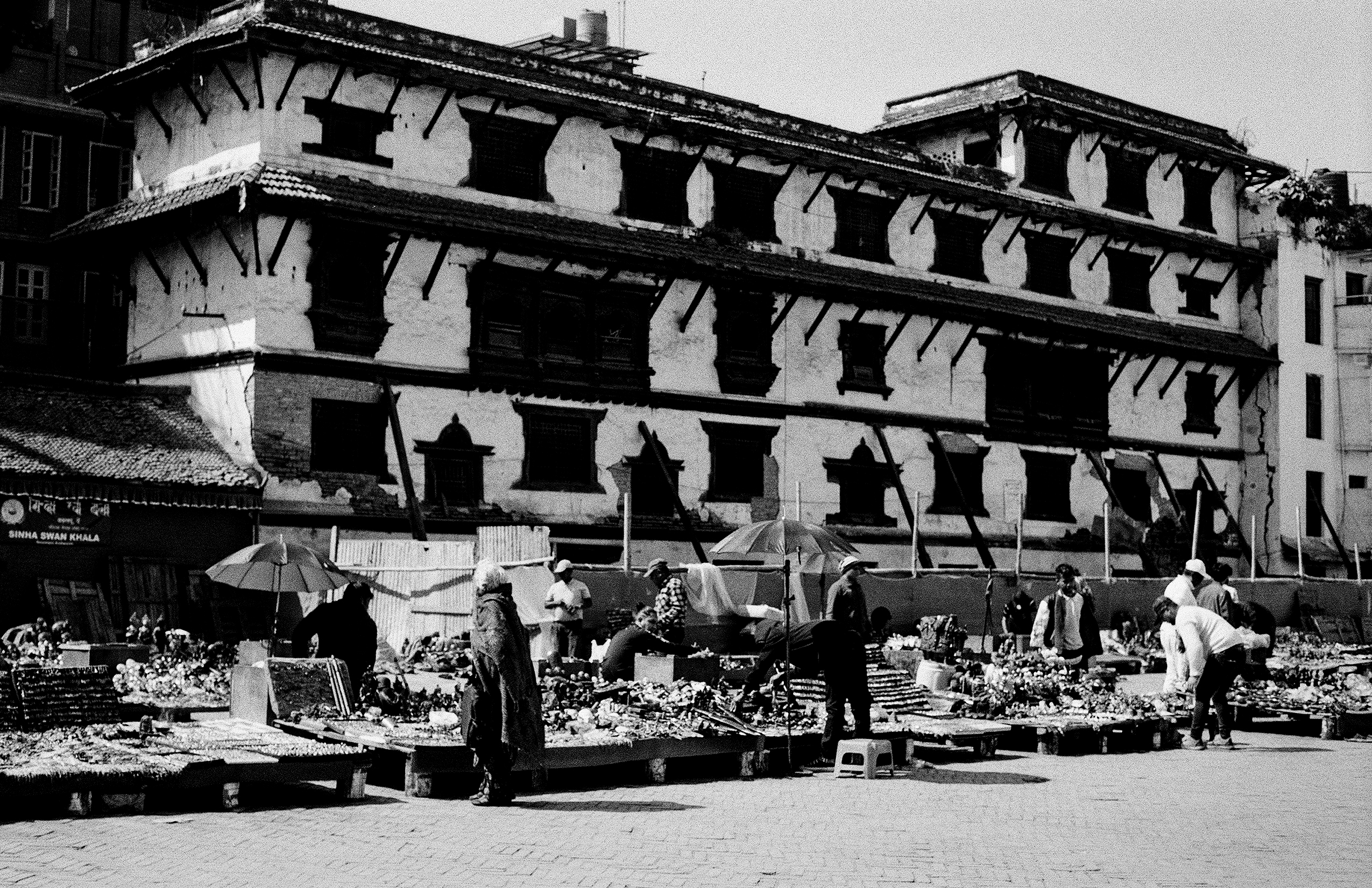 Bustling market scene at Durbar Square with flower sellers under umbrellas near colonial architecture