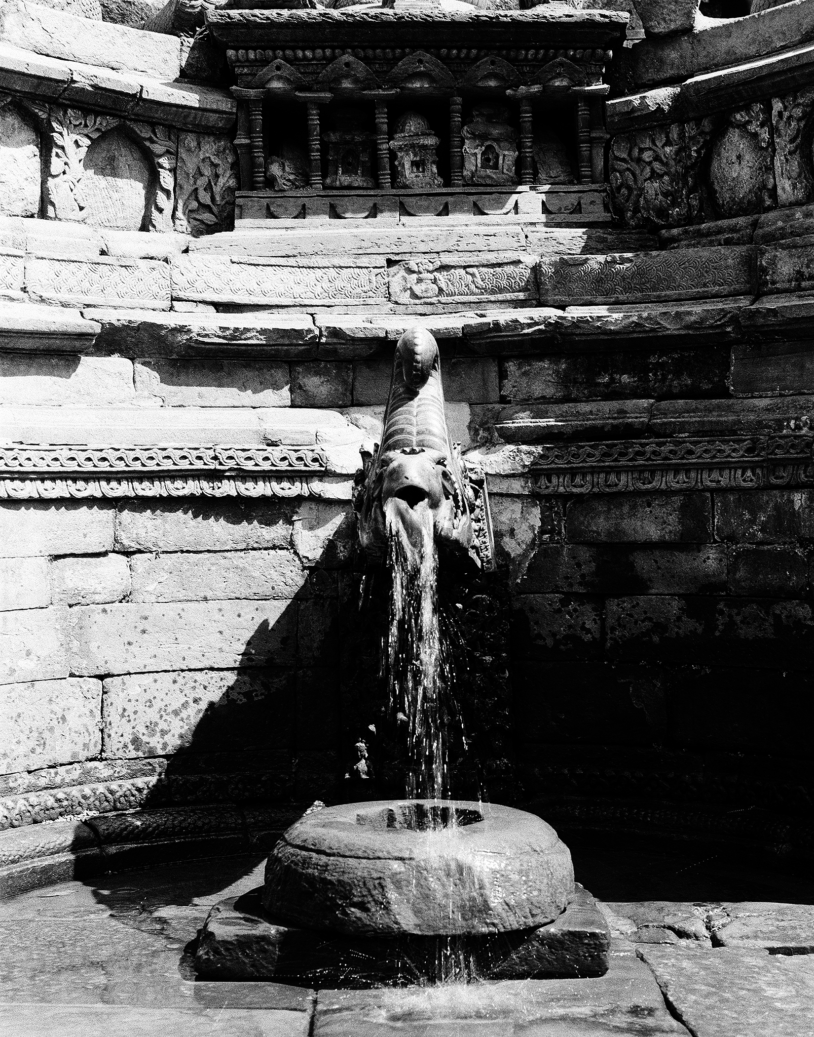 Water spout carved as ornate lion or makara head sculpture with flowing water at temple courtyard