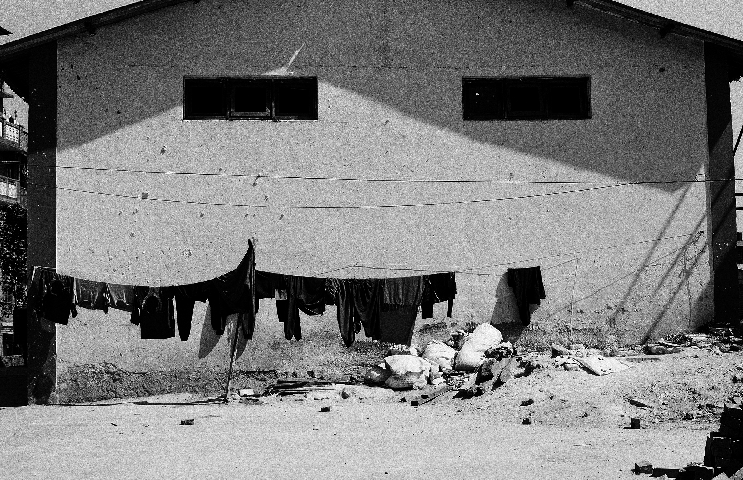 Clothesline of dark laundry casting dramatic shadow on white concrete courtyard wall