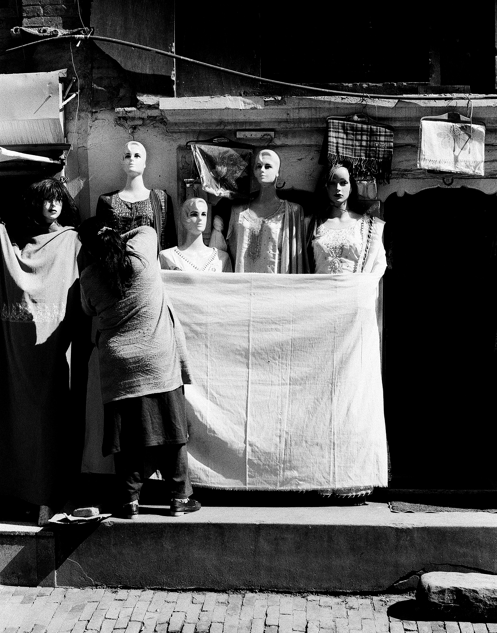 Multiple display mannequins wearing various traditional Nepali garments with colorful fabrics and laundry hanging behind