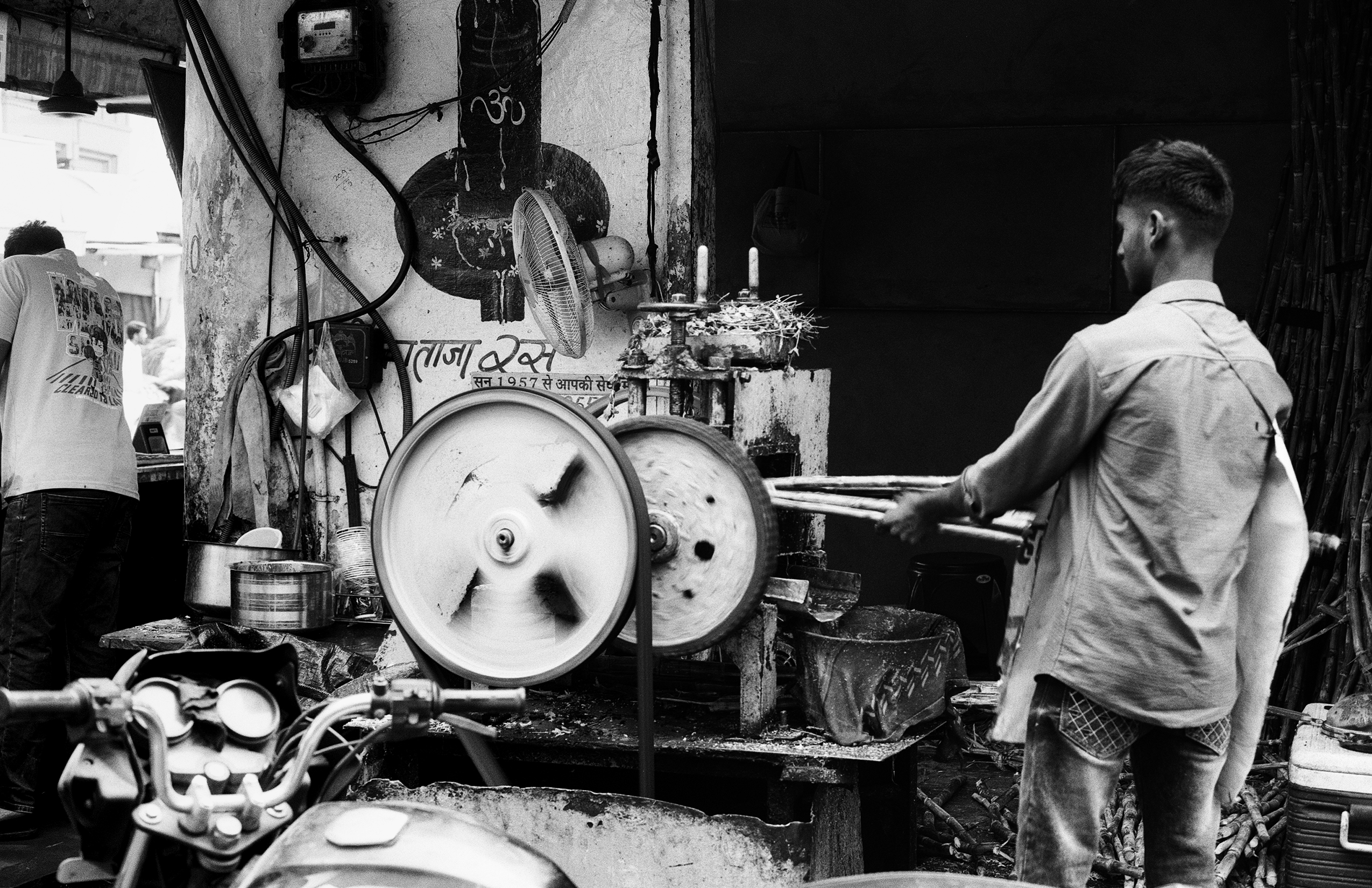 Black and white man operating sugarcane juice press with spinning flywheel and bamboo stalks