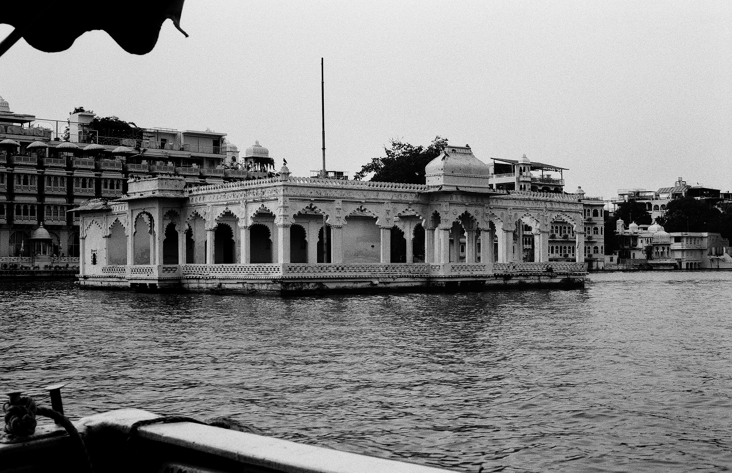Black and white white palace pavilion on Lake Pichola with arched colonnade and cityscape behind