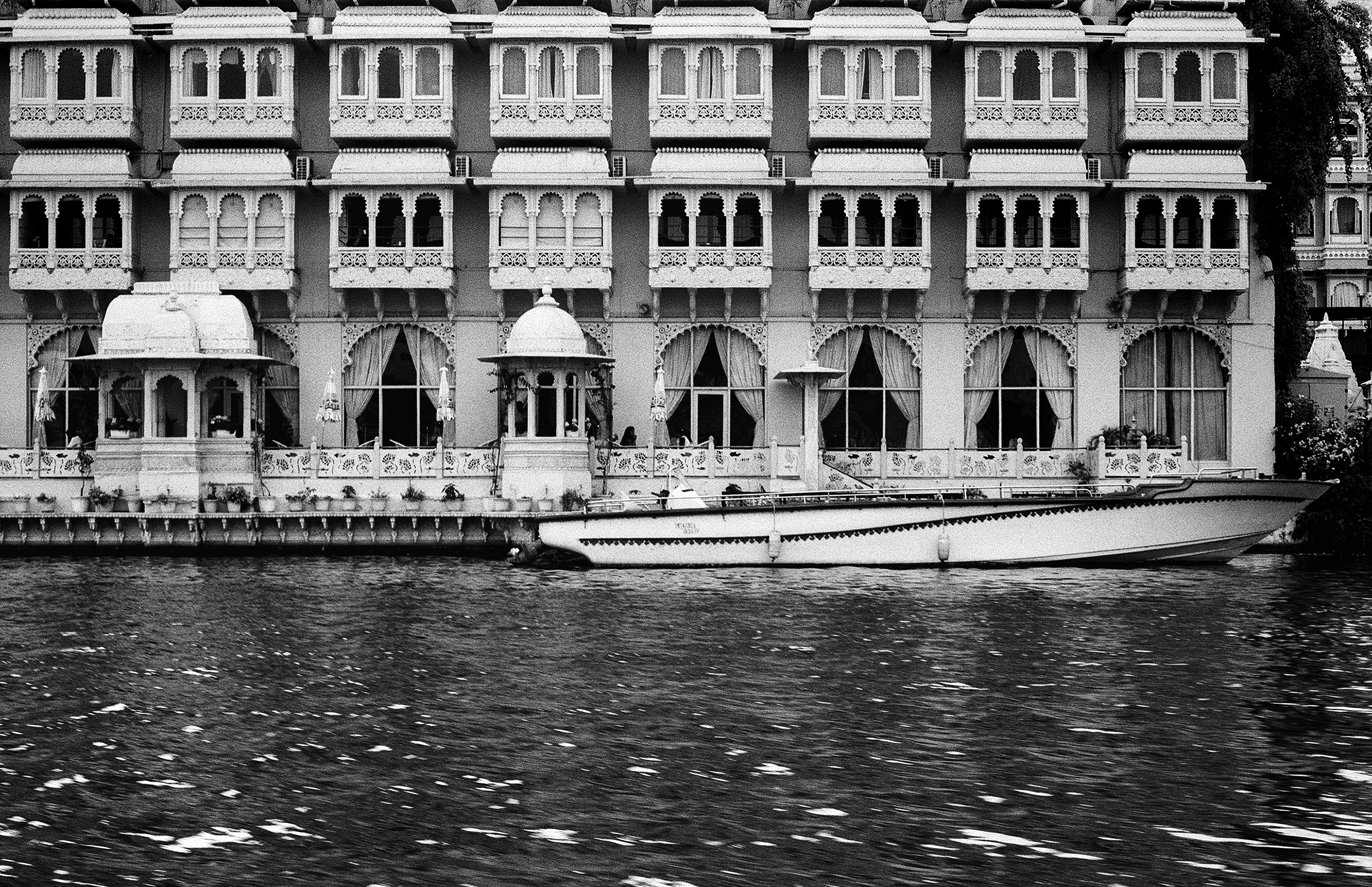 Black and white Lake Palace Hotel facade with ornate arched windows balconies and boat docked