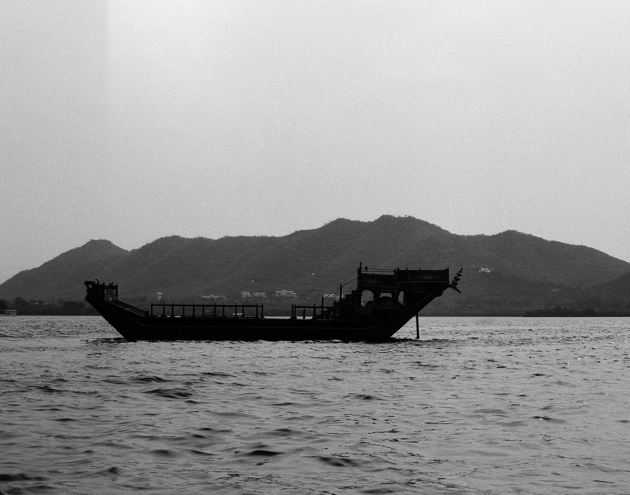 Black and white traditional wooden boat silhouette on lake with mountains in background