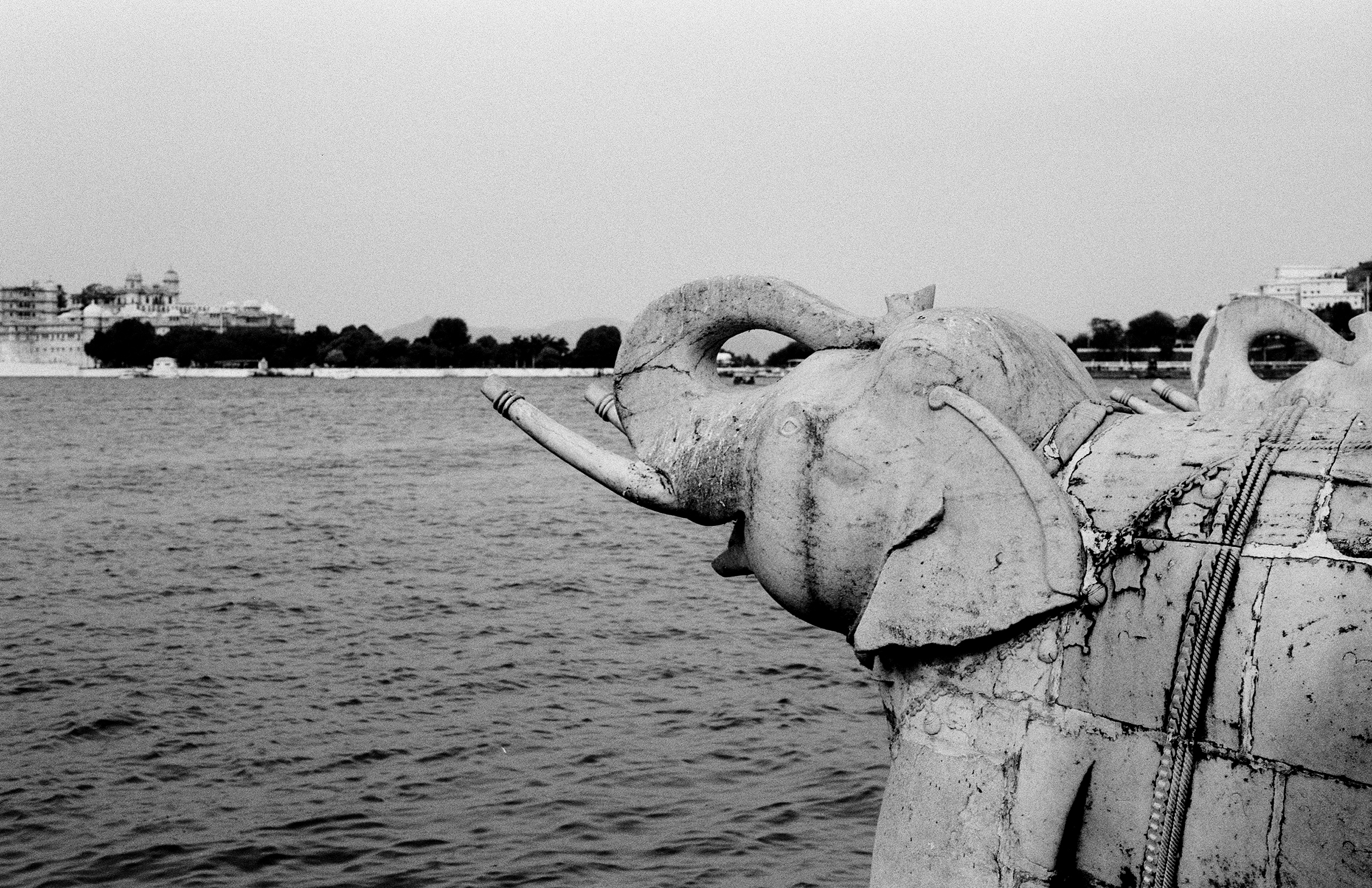 Black and white stone elephant head sculptures at water edge with lake and palace in background
