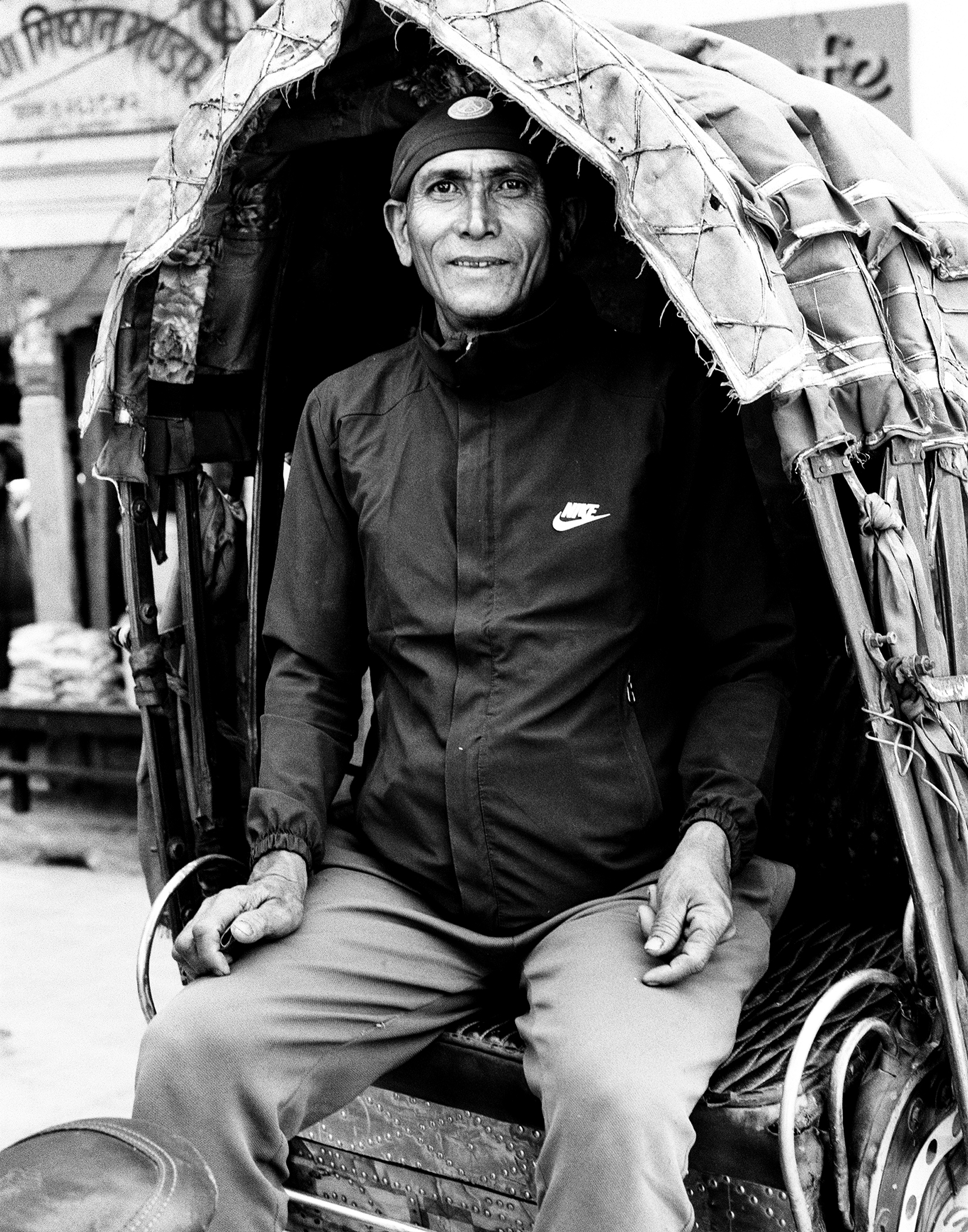 Smiling Nepali porter wearing Nike jacket sitting in traditional doko carrier basket with head straps