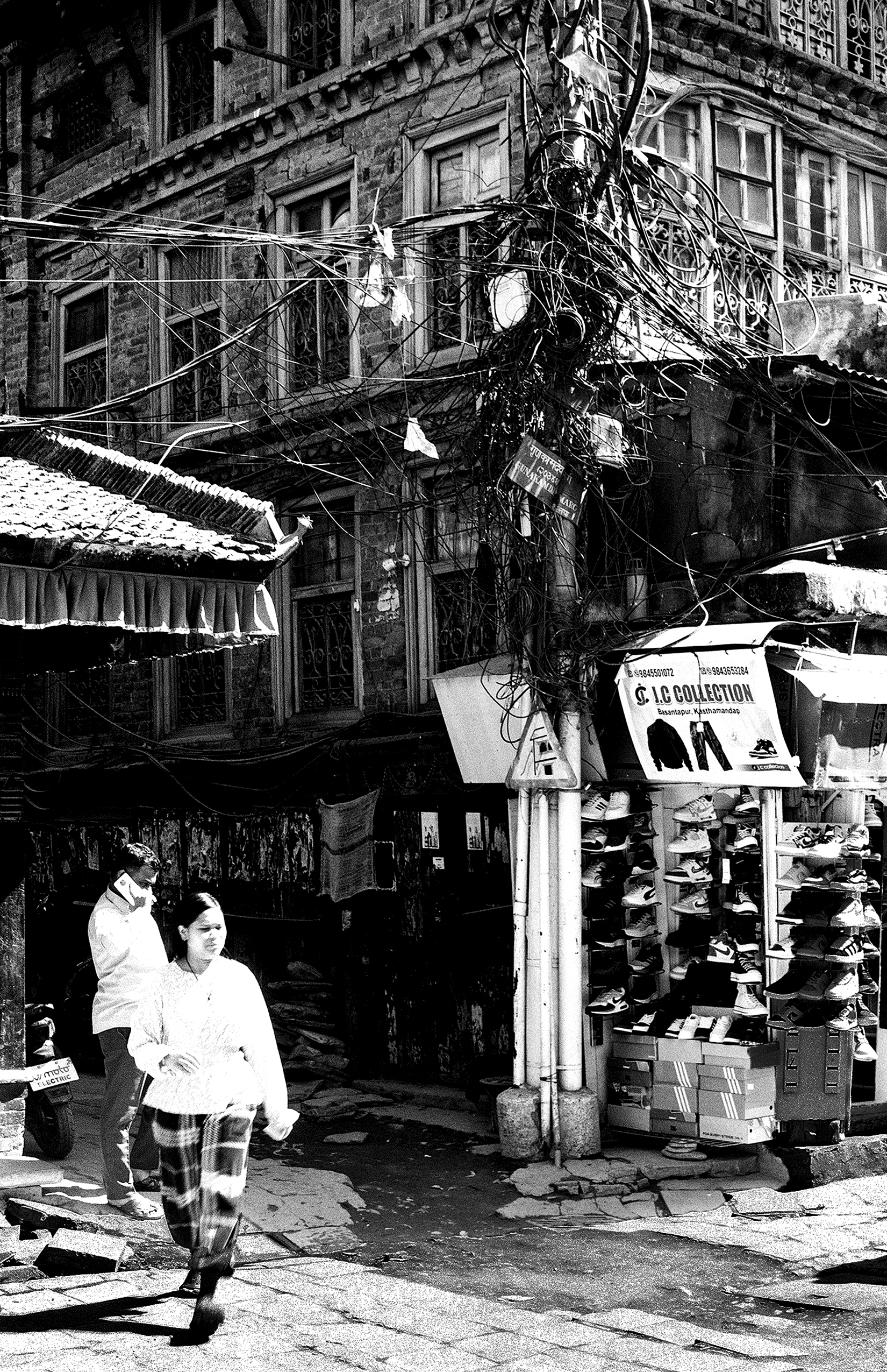 Kathmandu street scene with people walking past shop displaying shoes with tangled power lines overhead