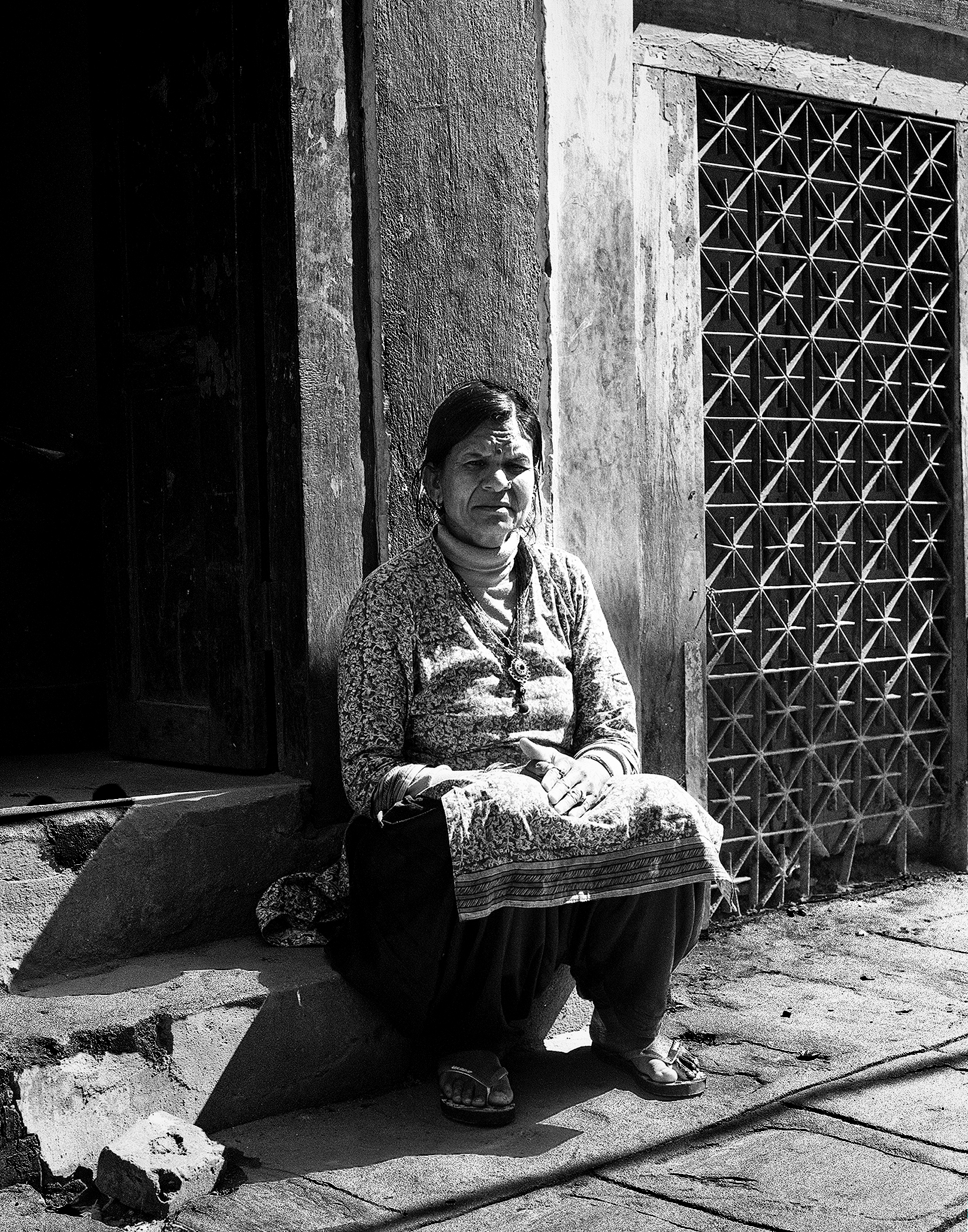 Nepali woman in traditional embroidered dress sitting at ornate geometric metal lattice doorway