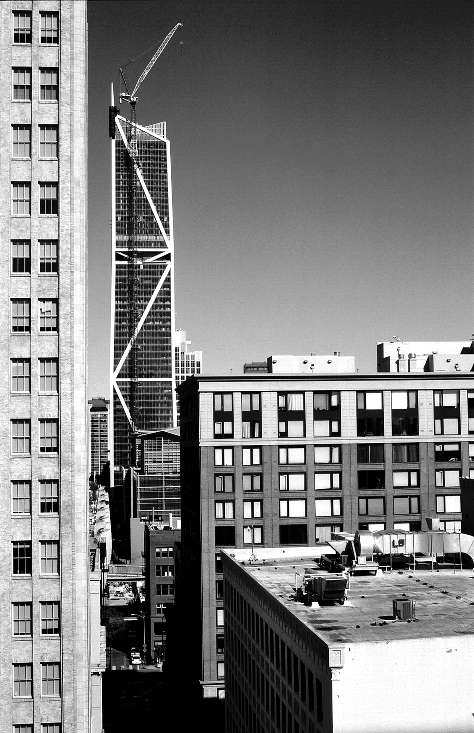 Vertical urban composition showing construction crane and modern steel building framework rising above older institutional architecture