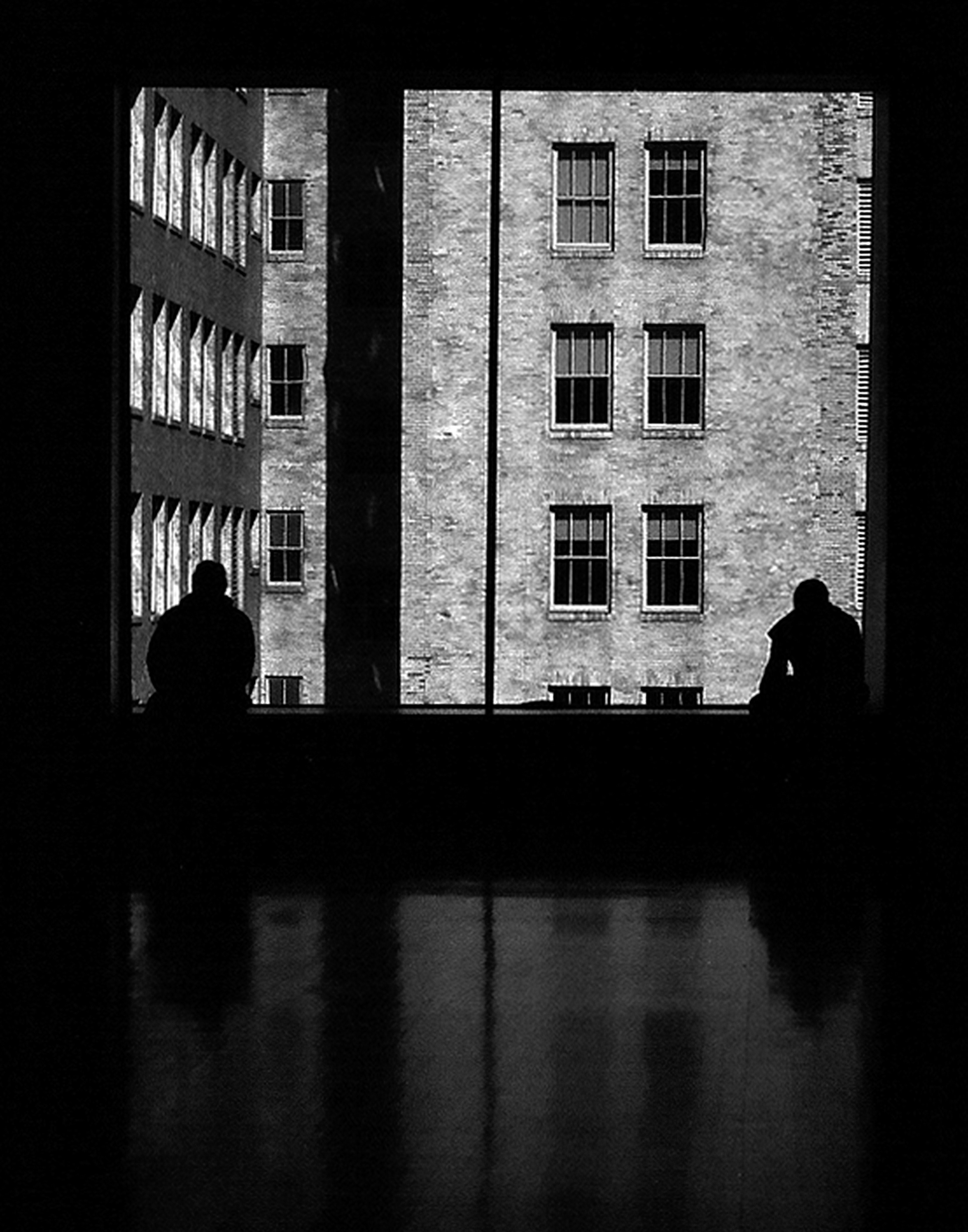 Two silhouetted figures framed through alley windows with opposing architectural facades creating dramatic light and shadow composition