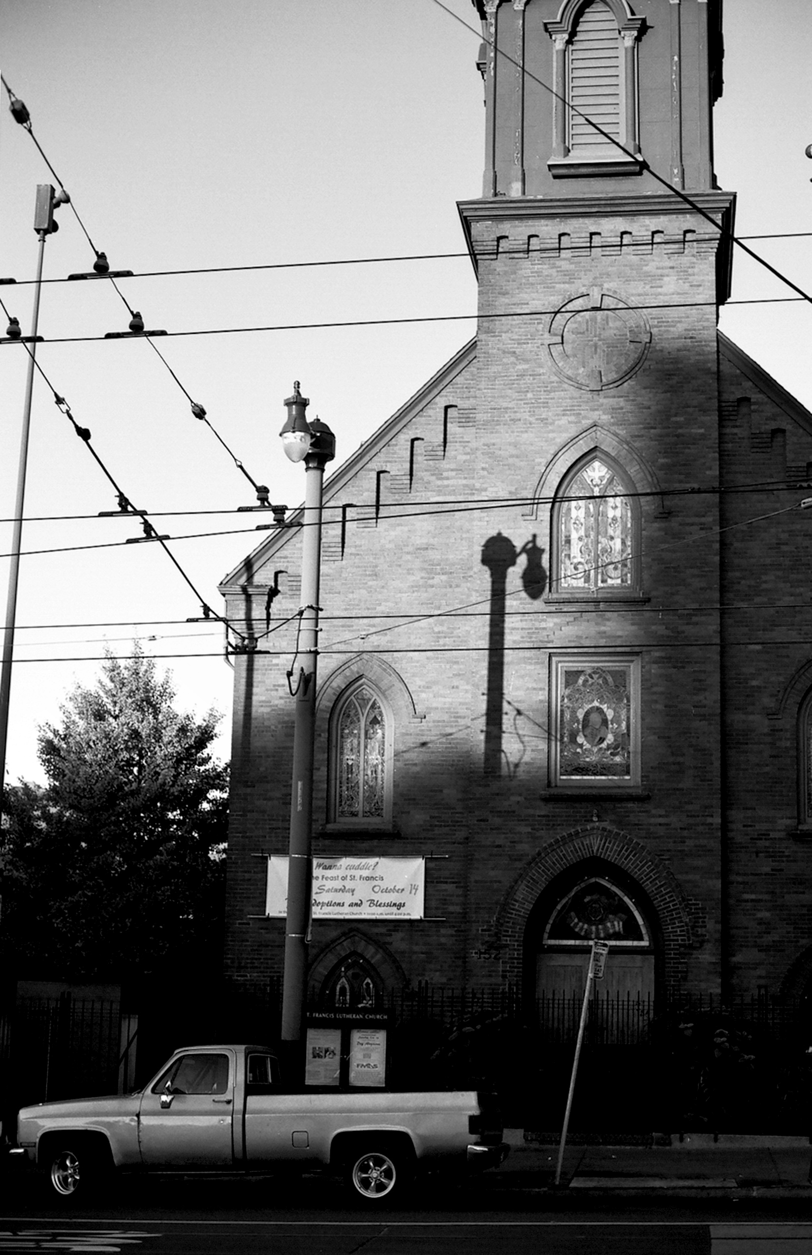 Historic church facade with Gothic arched windows stained glass power lines and vintage pickup truck on quiet street
