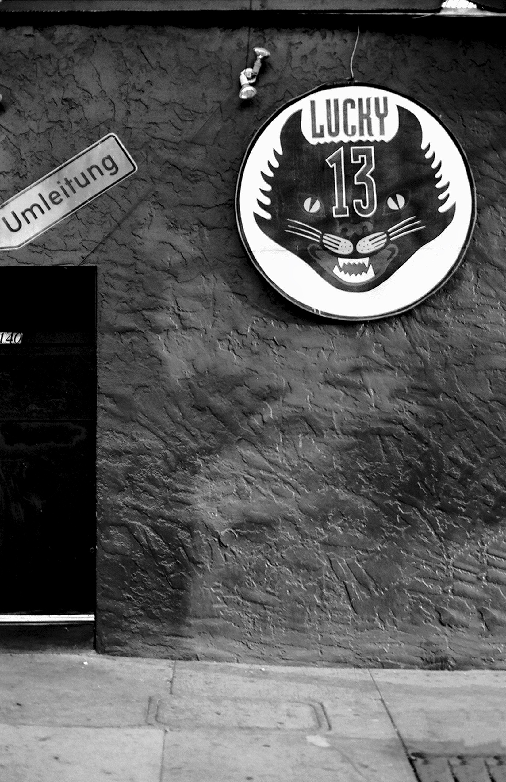 Lucky 13 tiger face sign on weathered concrete wall with Umleitung detour sign and mailbox creating quirky urban vernacular detail