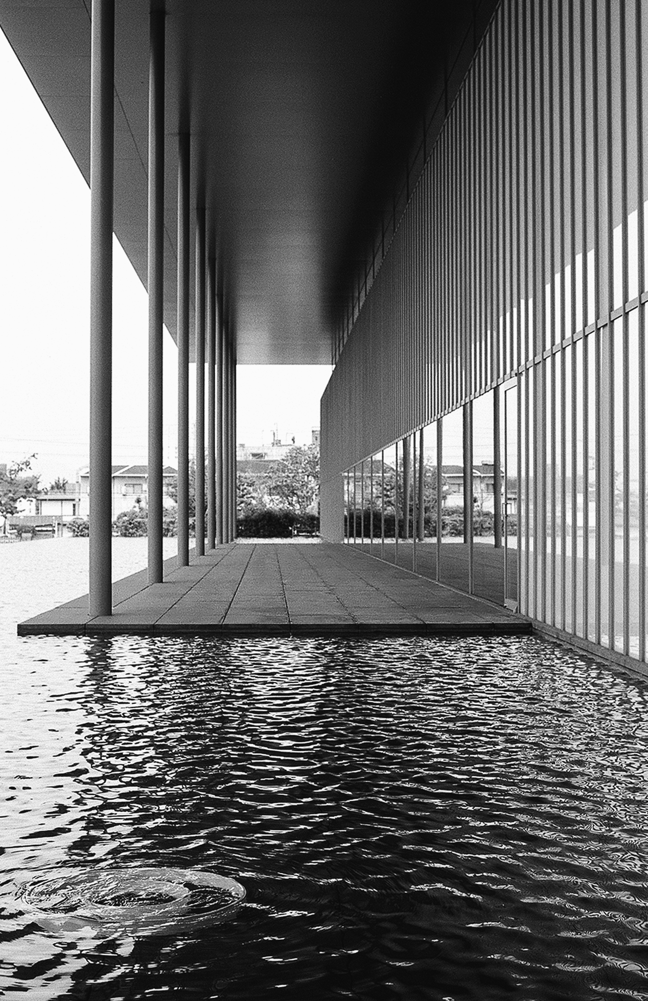 Architectural passage beneath modern structure with vertical metal railings reflecting in water and textured flooring