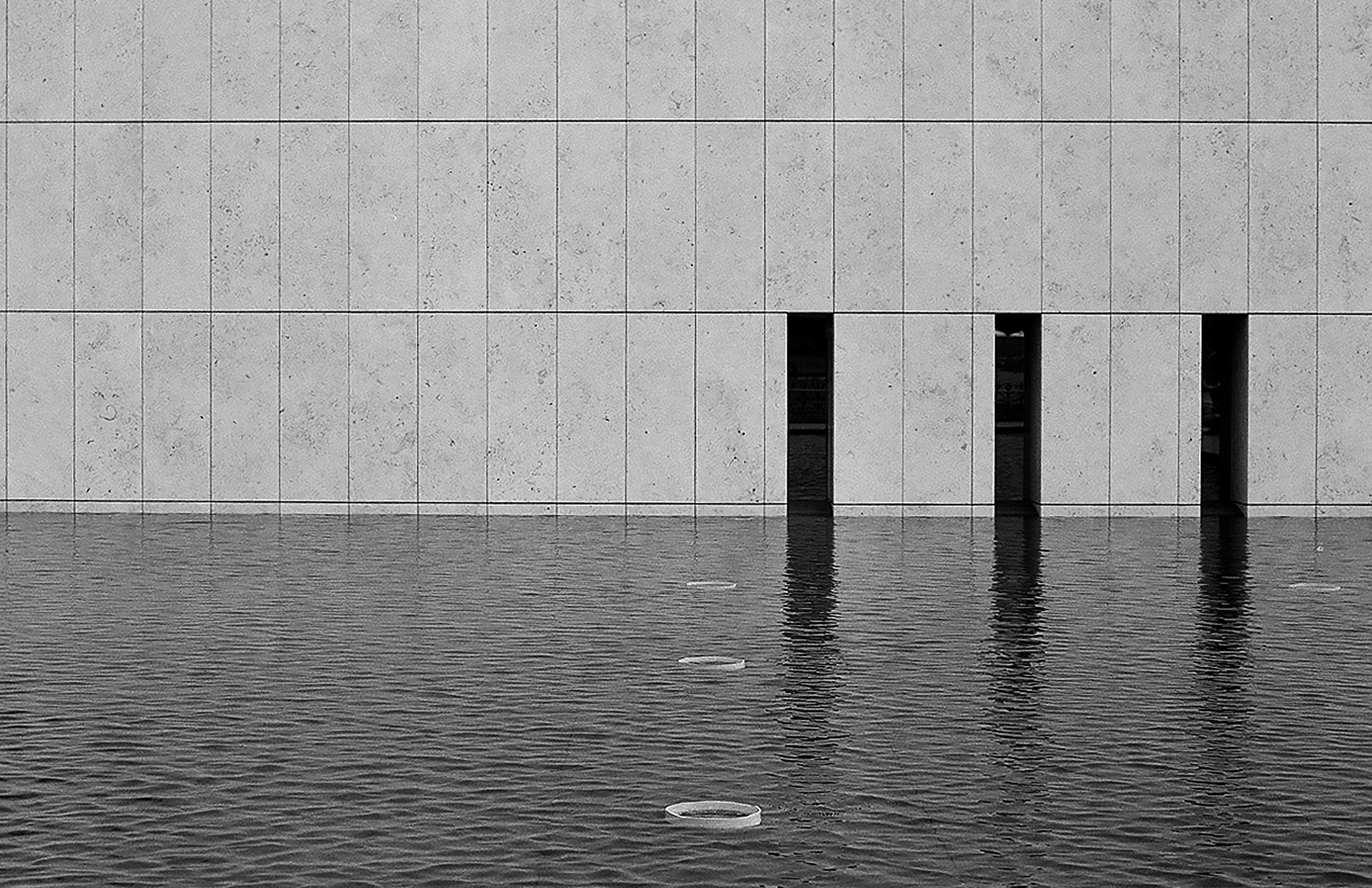 Minimalist water reflection of concrete grid facade with three rectangular dark openings under geometric panel divisions
