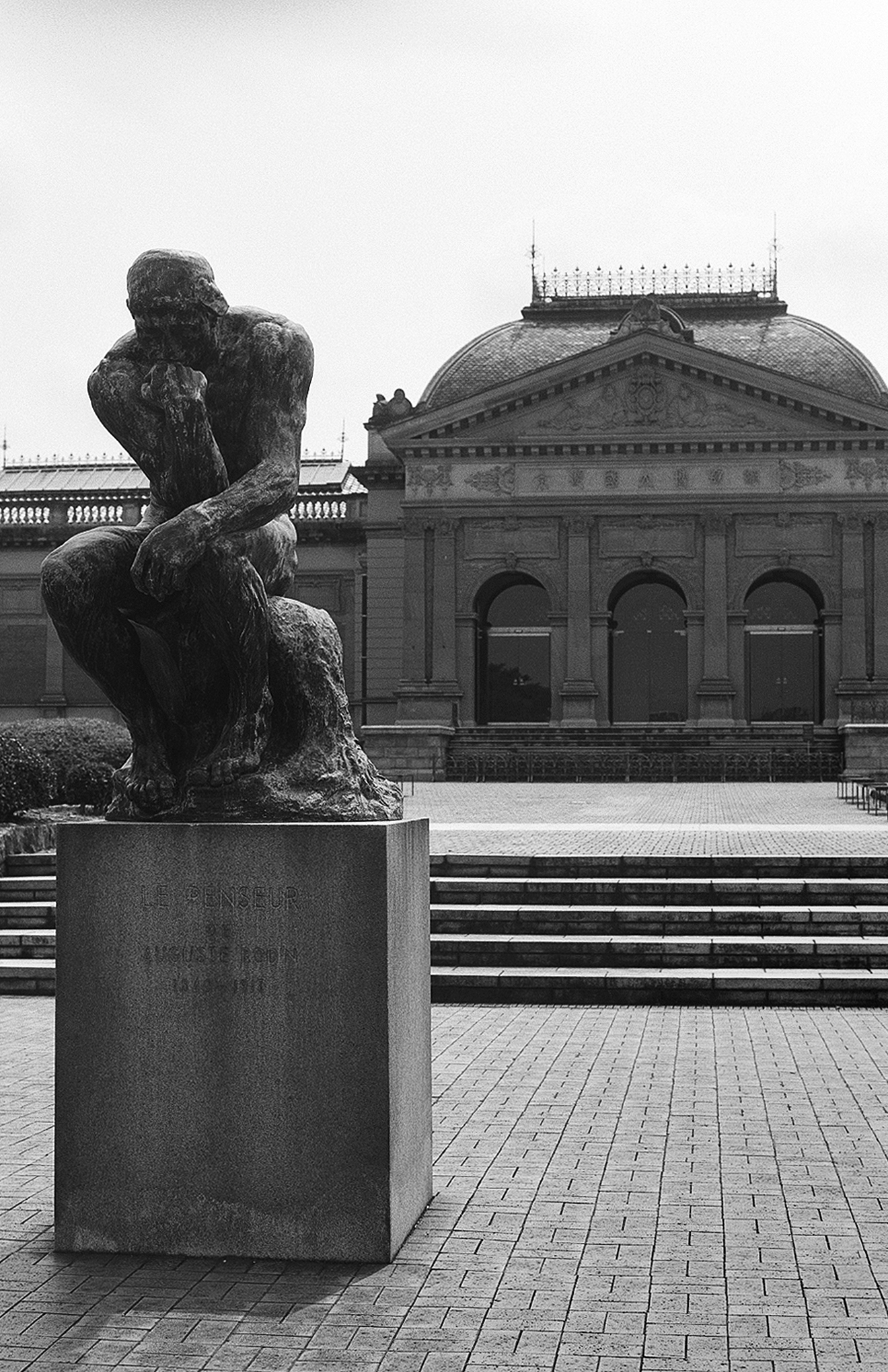 Rodin Thinker sculpture before neoclassical dome building with manicured grounds and maturing trees