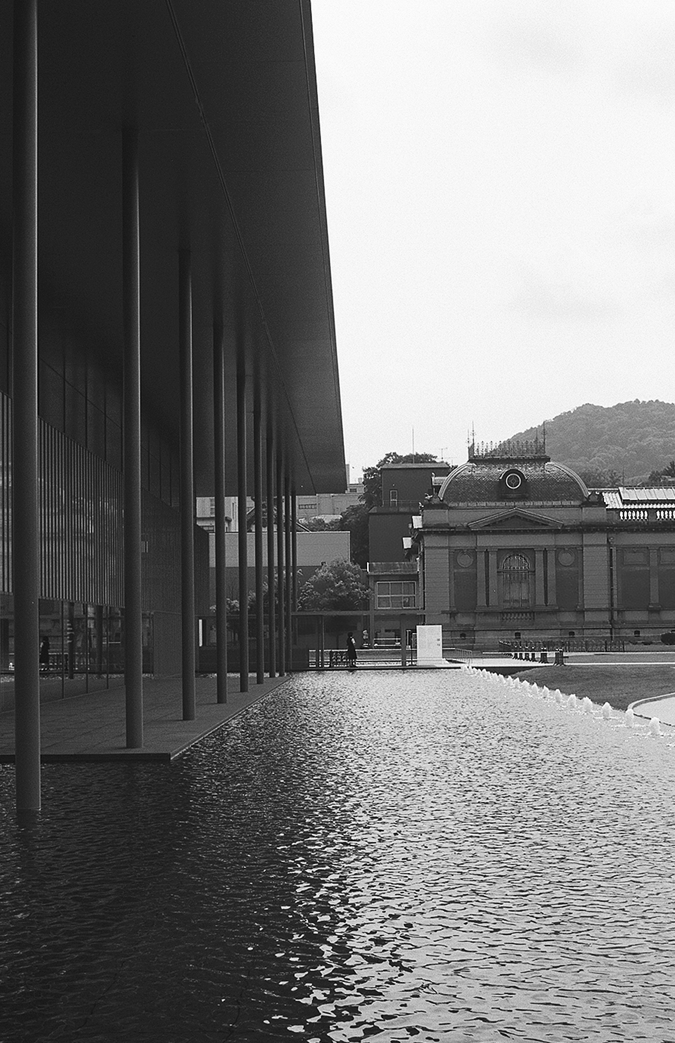 Modern museum building with horizontal window blinds beside reflective water and forested mountainside background