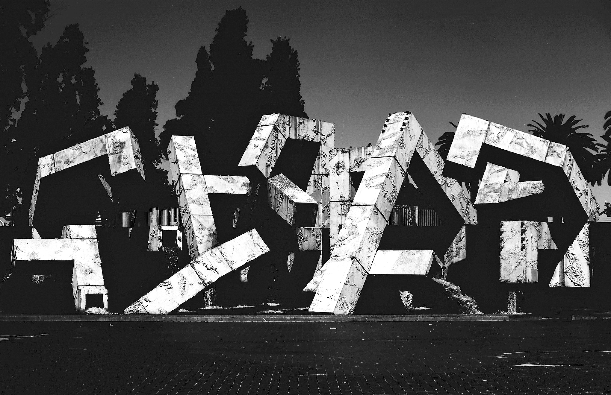 Vaillancourt Fountain brutalist concrete sculpture with angular geometric forms silhouetted trees and palm in Embarcadero plaza