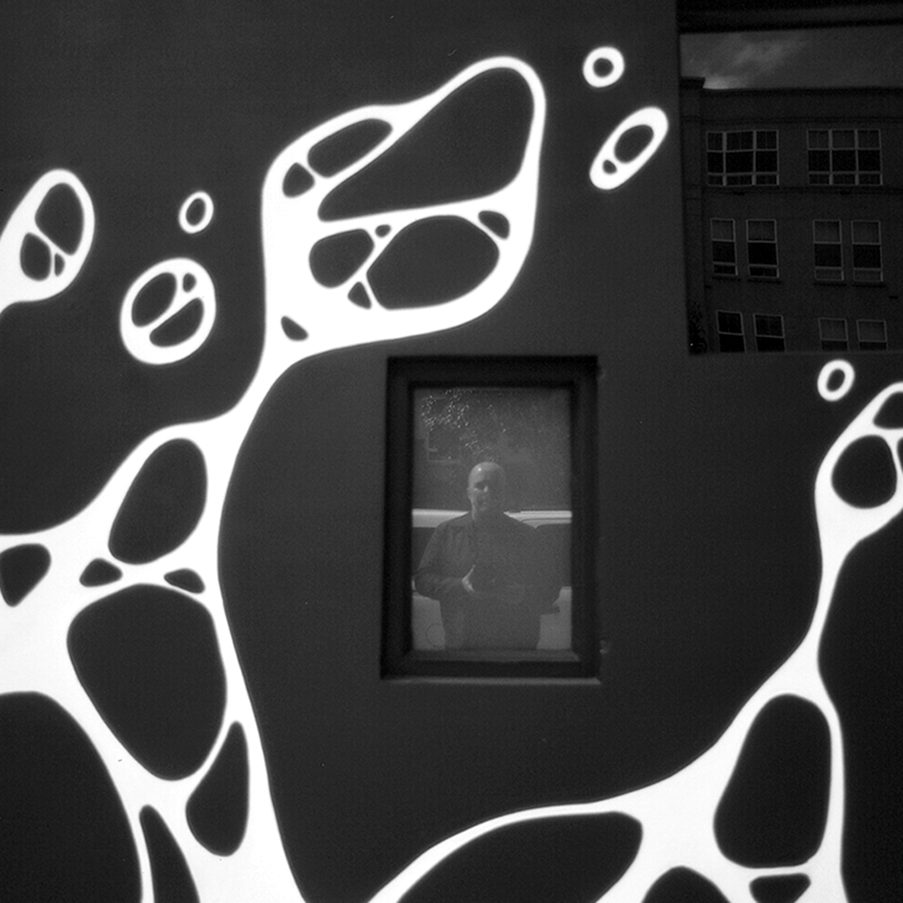 Building facade with abstract white organic bubble mural on dark wall person silhouette visible through window