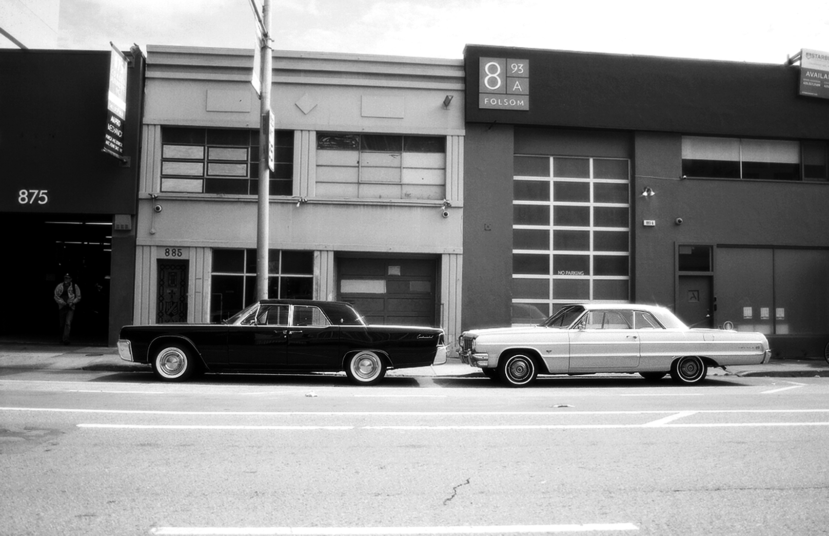 Two vintage cars from 1960s parked on street with historic warehouse buildings and Folsom sign