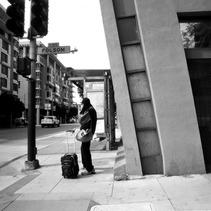 Person with luggage standing at street corner under Folsom sign with traffic light