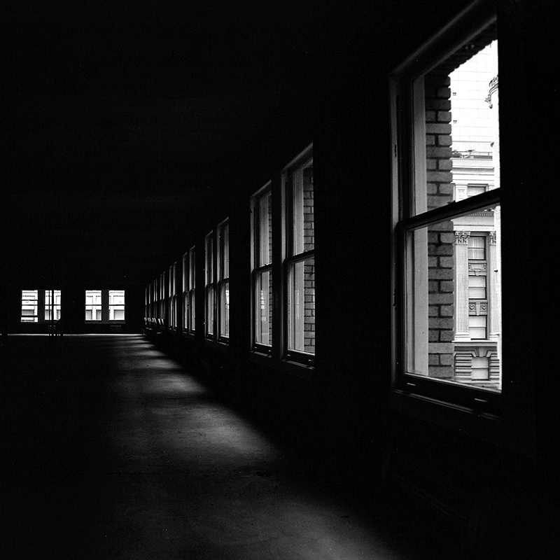 Dark interior corridor with row of bright windows on right showing exterior cityscape