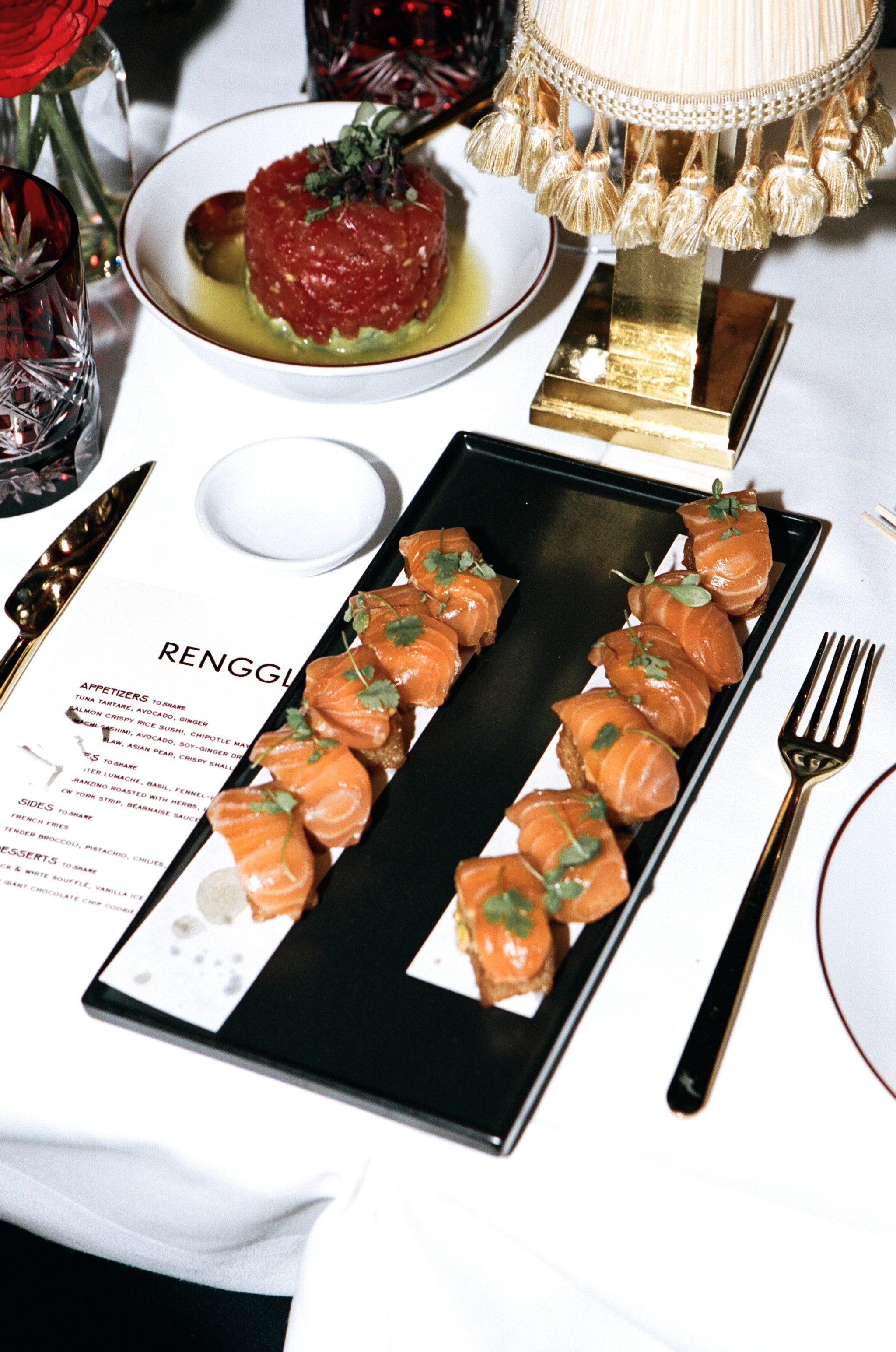 Elegant restaurant table with tuna tartare, salmon crispy rice, menu, and gold tasseled lamp