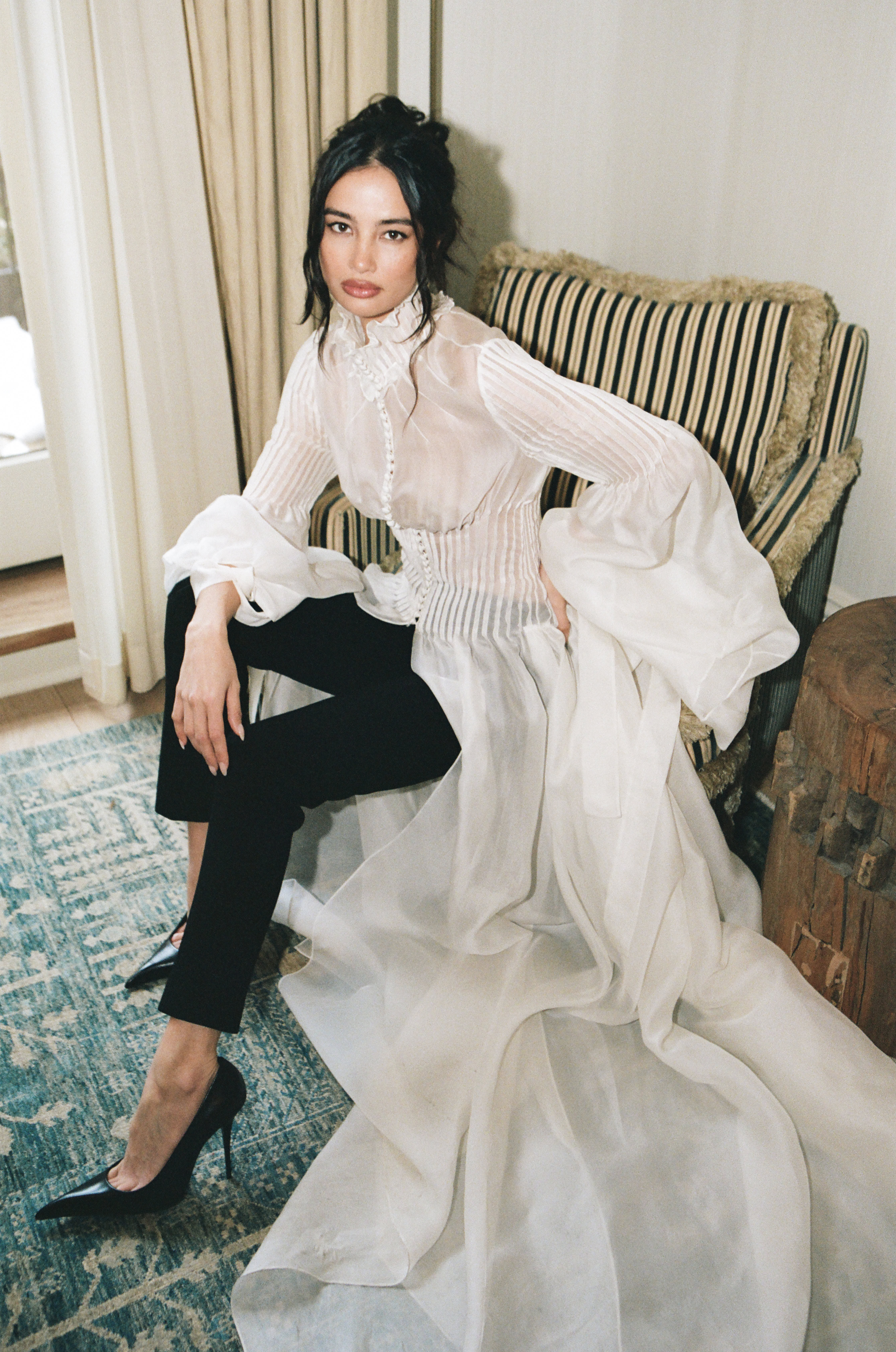 Woman sitting on striped sofa in flowing white button-up shirt and black pants
