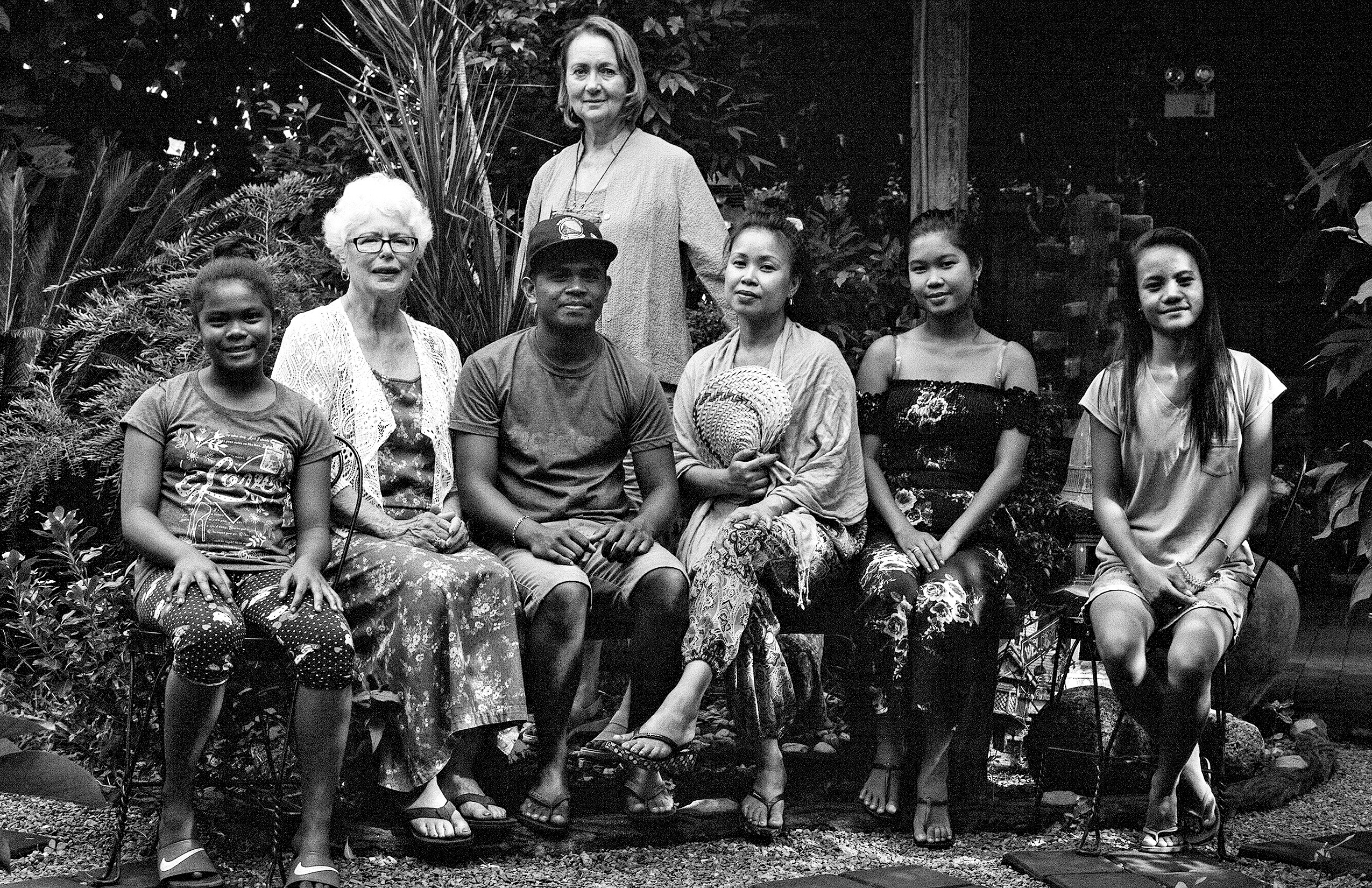 Multigenerational group portrait of seven people seated together in garden setting at night with lush foliage
