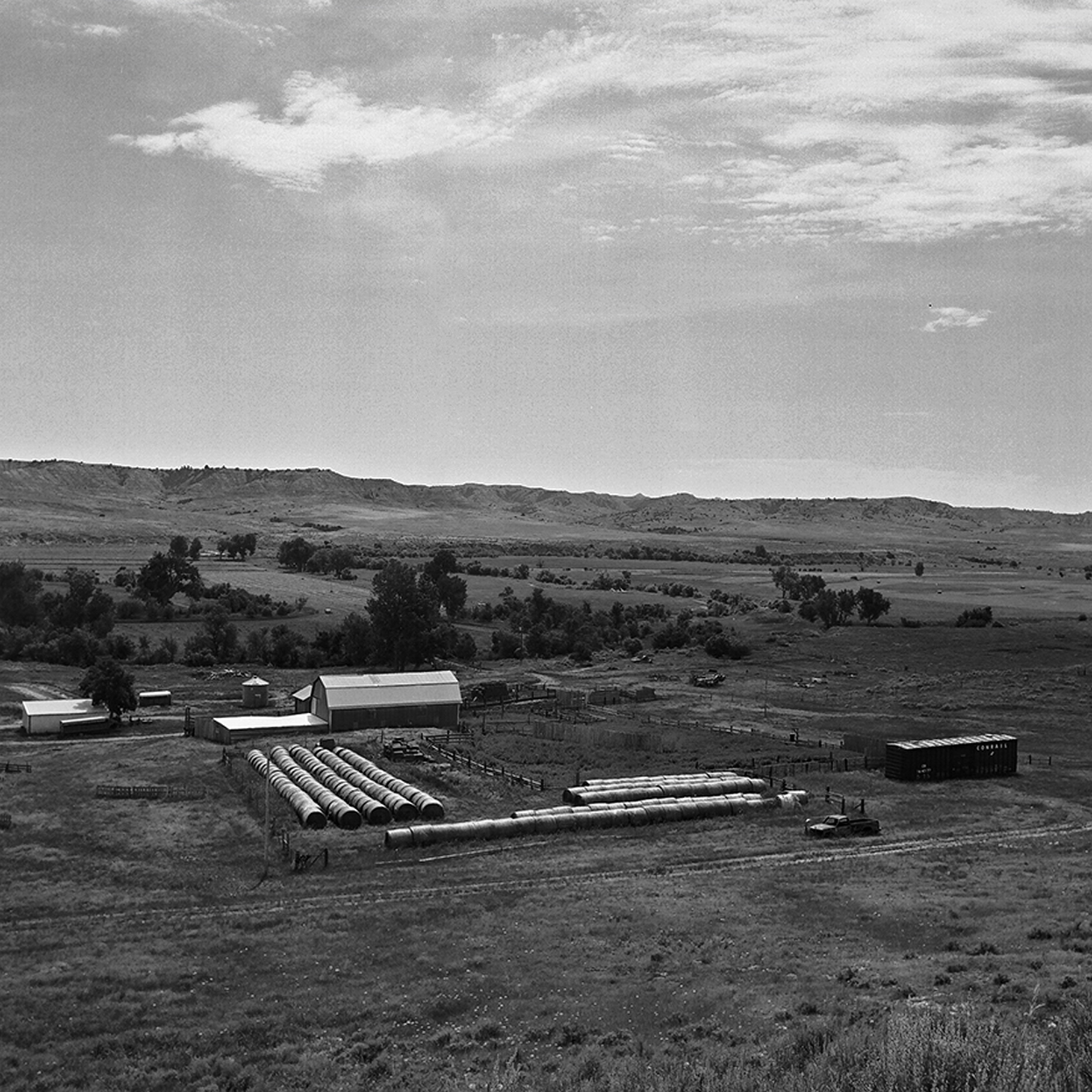 Aerial view of ranch with hay bale storage barn buildings and corrals set in rolling prairie hills
