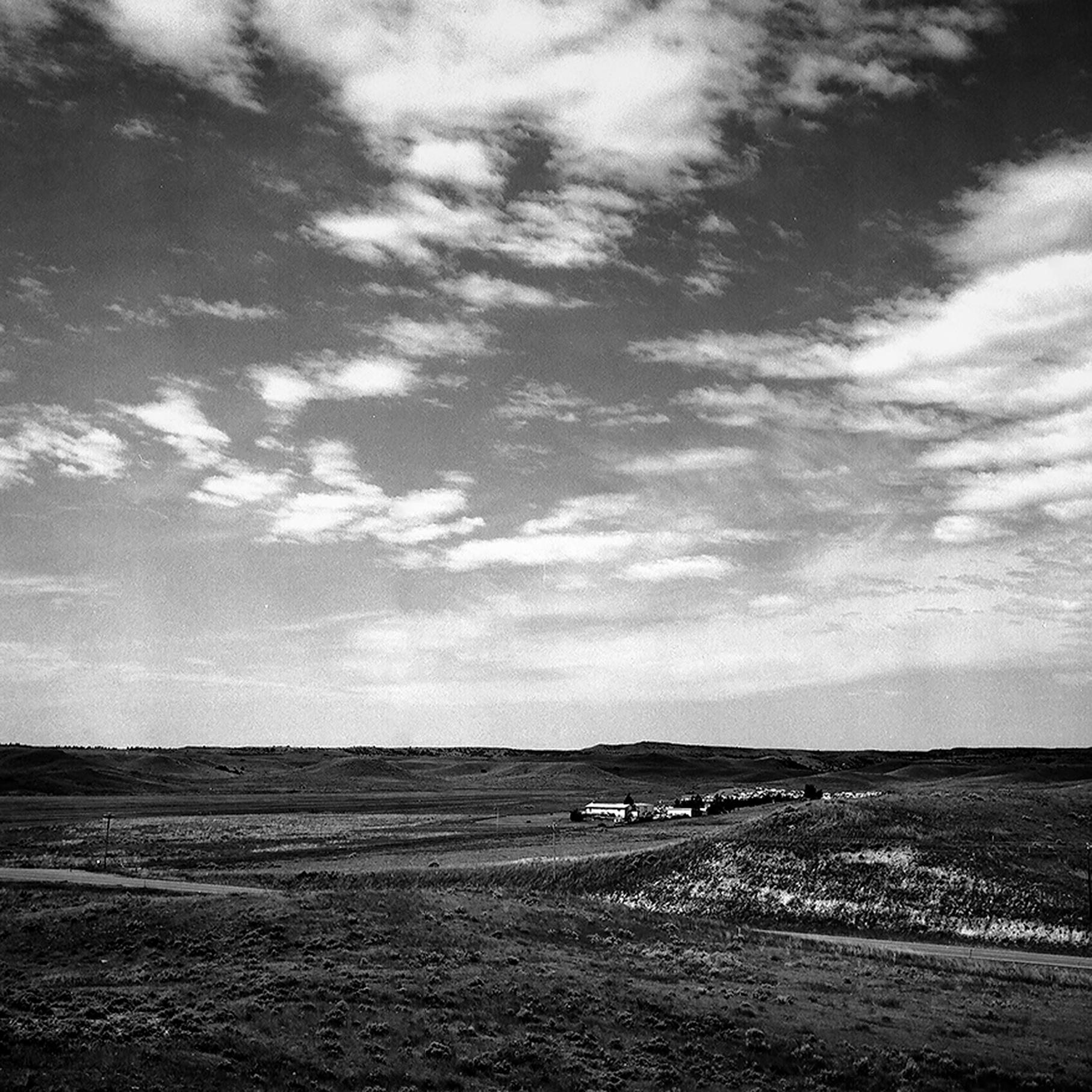Expansive prairie landscape with dramatic big sky clouds and isolated farm buildings in rolling hills distance