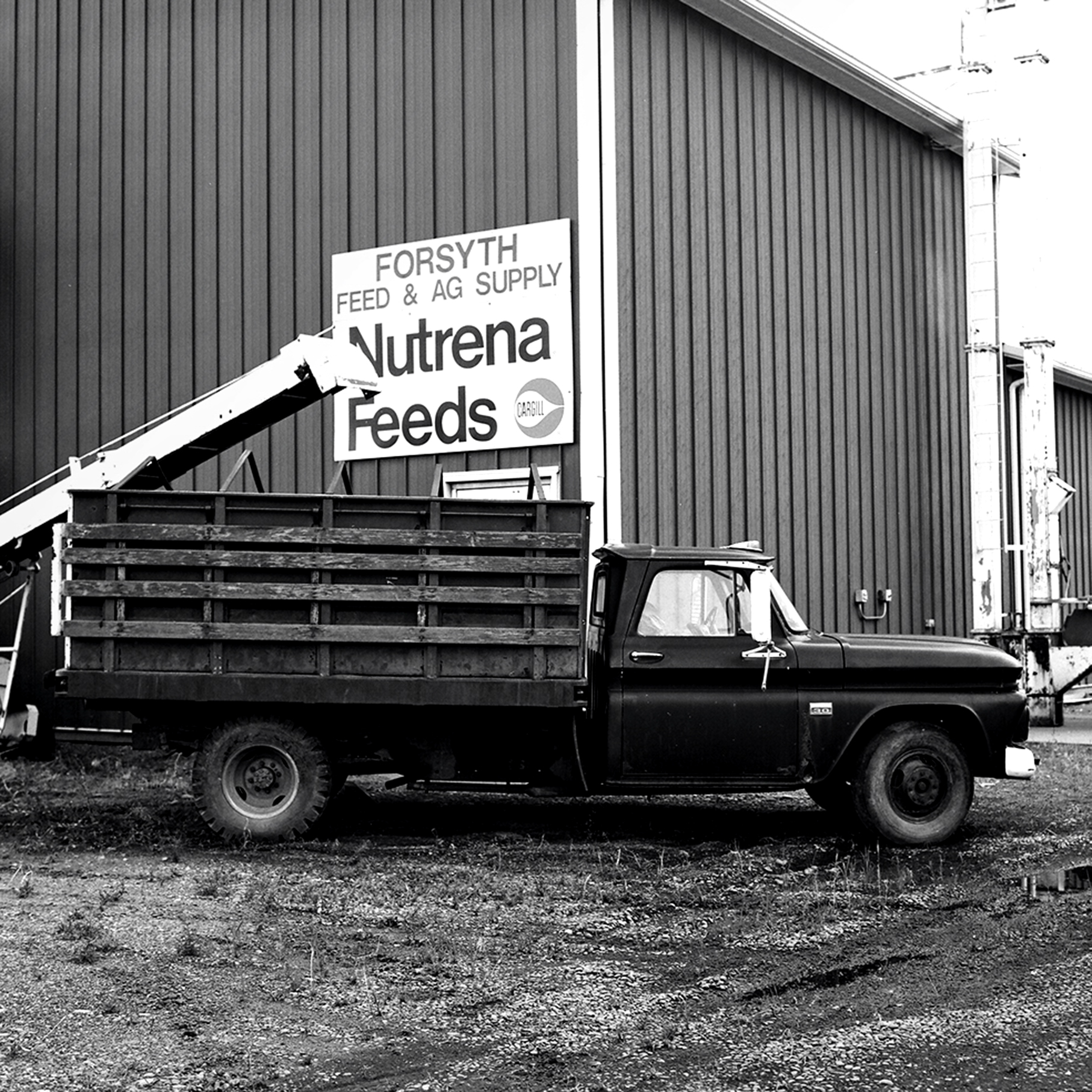 Vintage stake bed truck parked at Forsyth Feed and Ag Supply with Nutrena Feeds sign on corrugated metal building