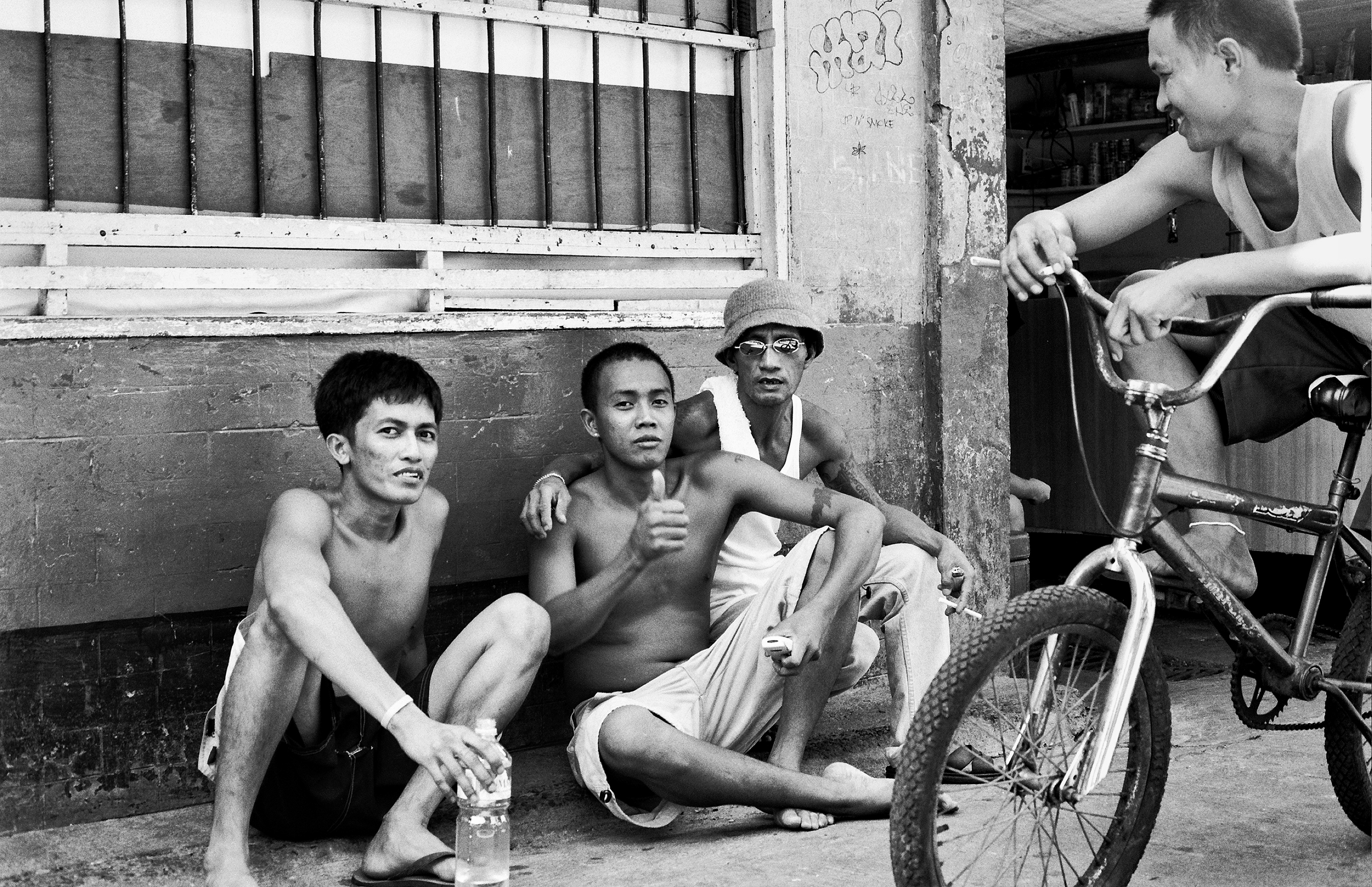 Three young men sitting on sidewalk with bicycle visible chatting in casual urban street scene