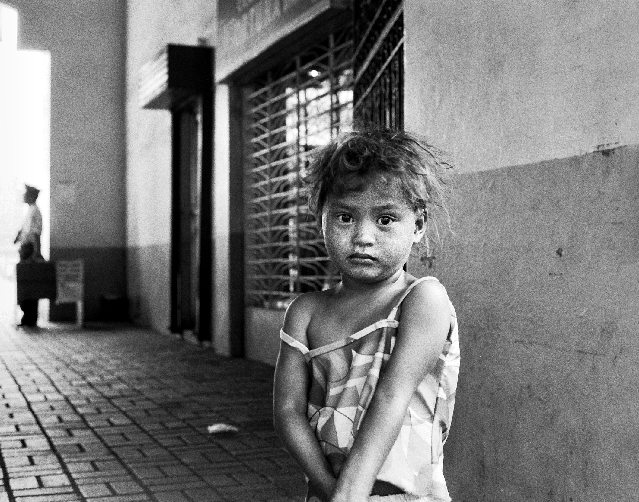 Young girl with tousled hair in patterned dress standing in urban alleyway looking directly at camera