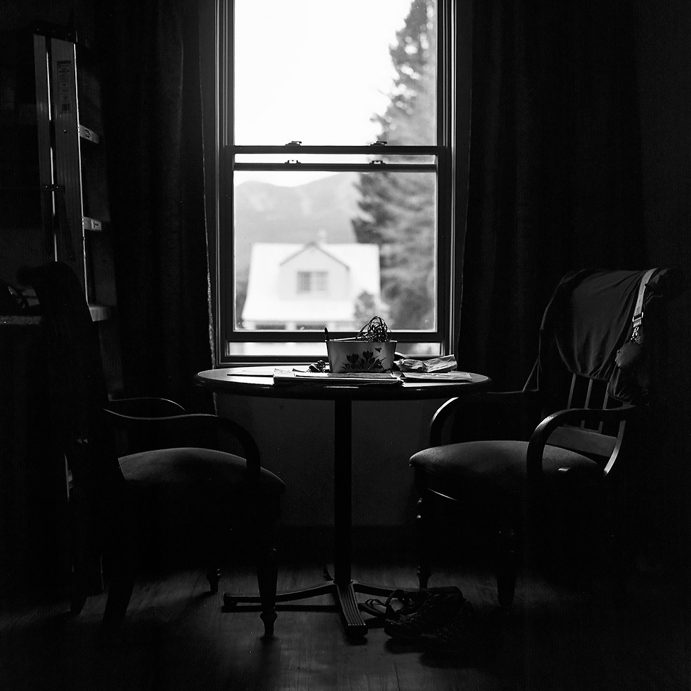 Intimate interior scene with bistro table and chairs silhouetted against window overlooking mountain town