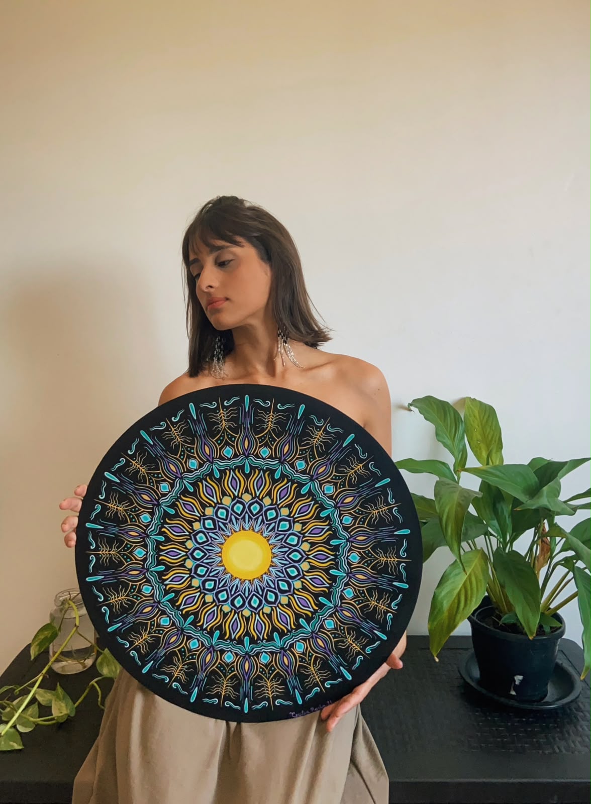 Cecília segurando mandala circular preta com turquesa, roxo e sol dourado no centro