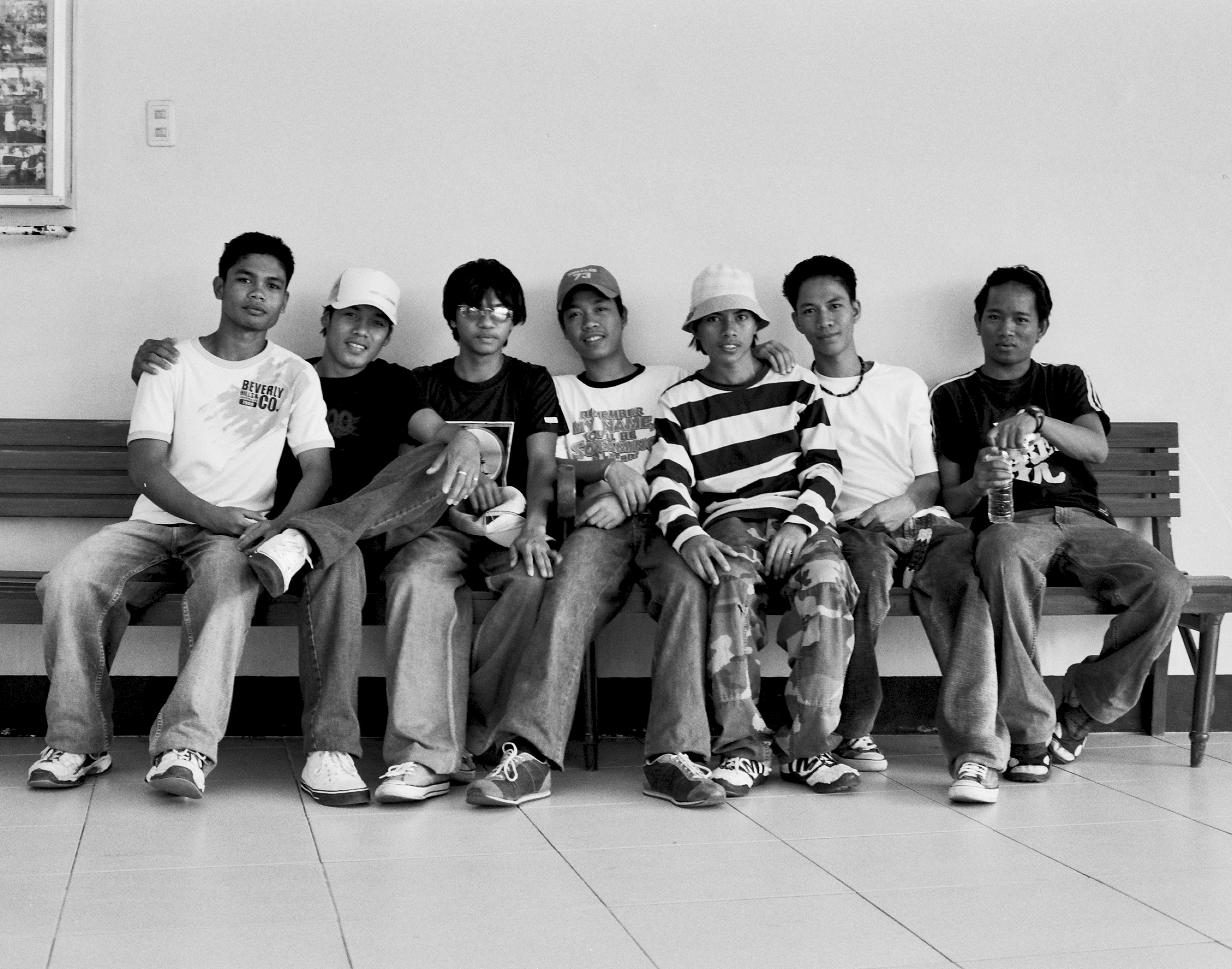 Group of seven young Filipino men sitting together on bench posed for group portrait indoors