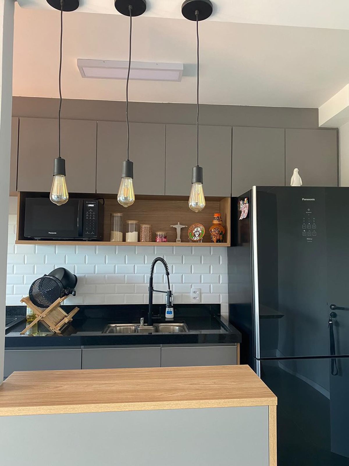 Cozinha com pendentes, armários cinza e bancada em madeira