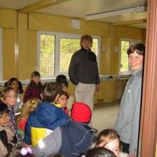 Zwei Erwachsene begrüßen eine Schulklasse im Container