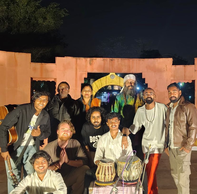 Musicians and spiritual community gathered at night for a peace concert, with guitars and tabla drums