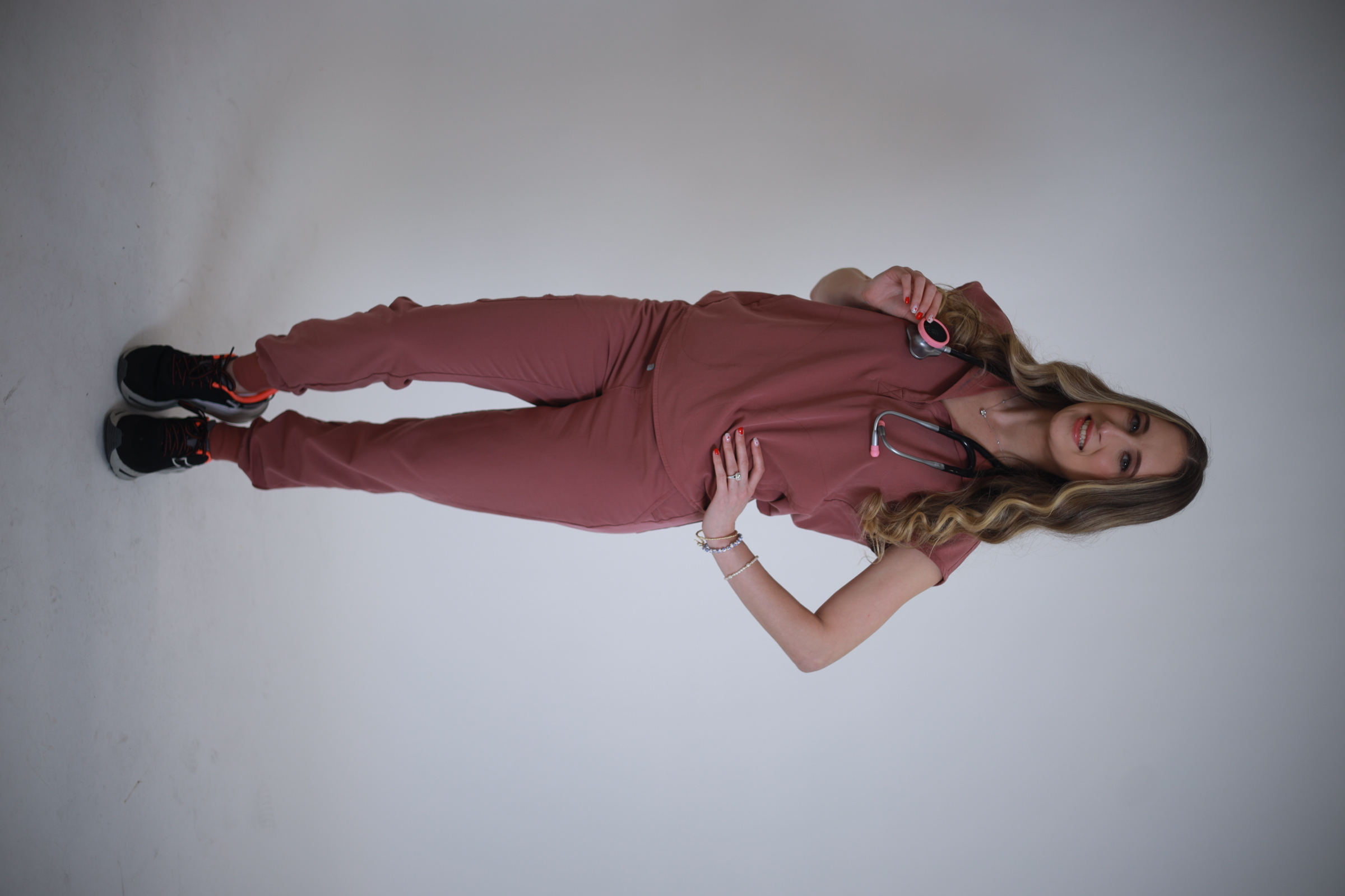 Yanelis standing in rosewood scrubs and sneakers holding a digital stethoscope