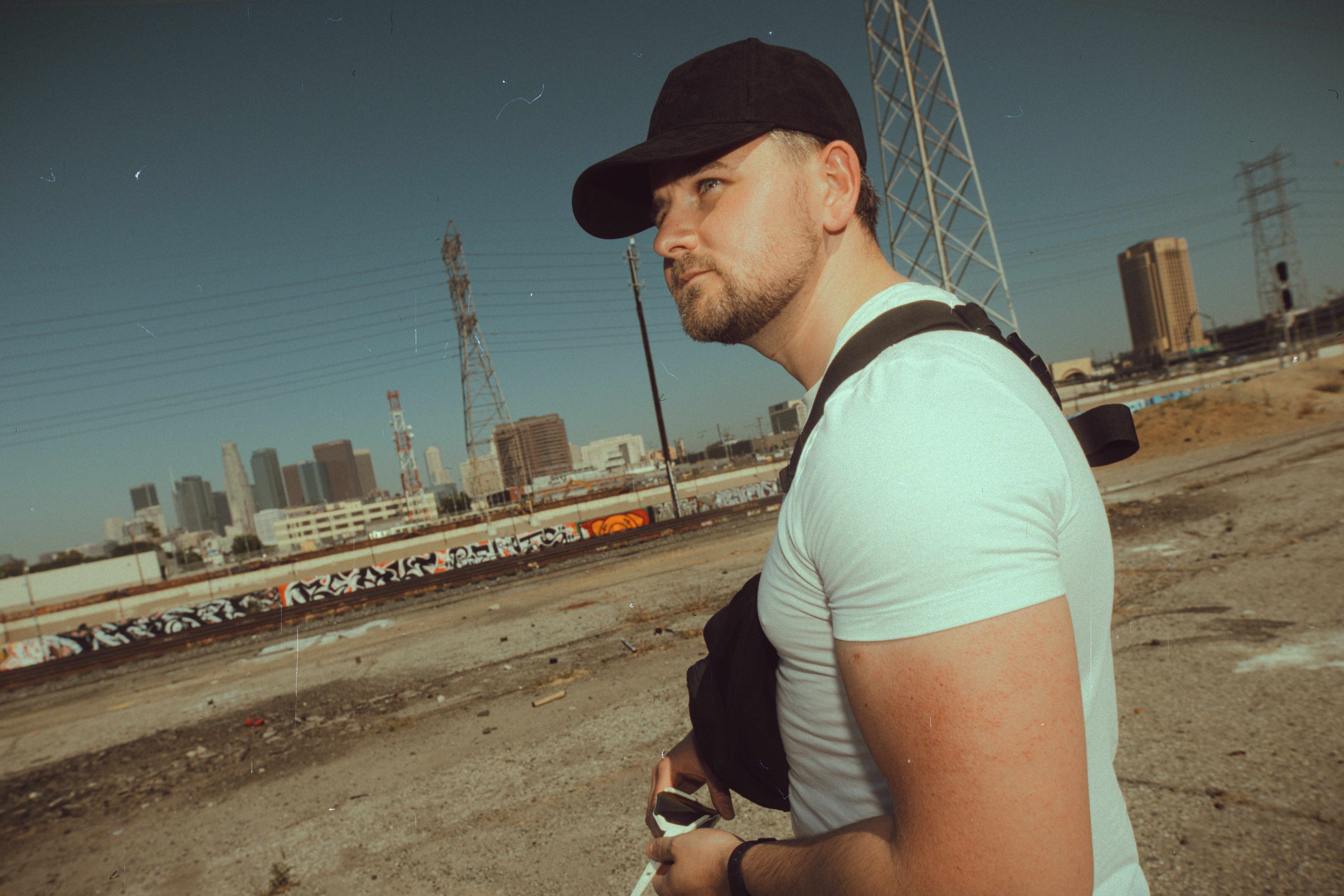 Emanuel Tschann in profile with a camera bag, industrial skyline behind him