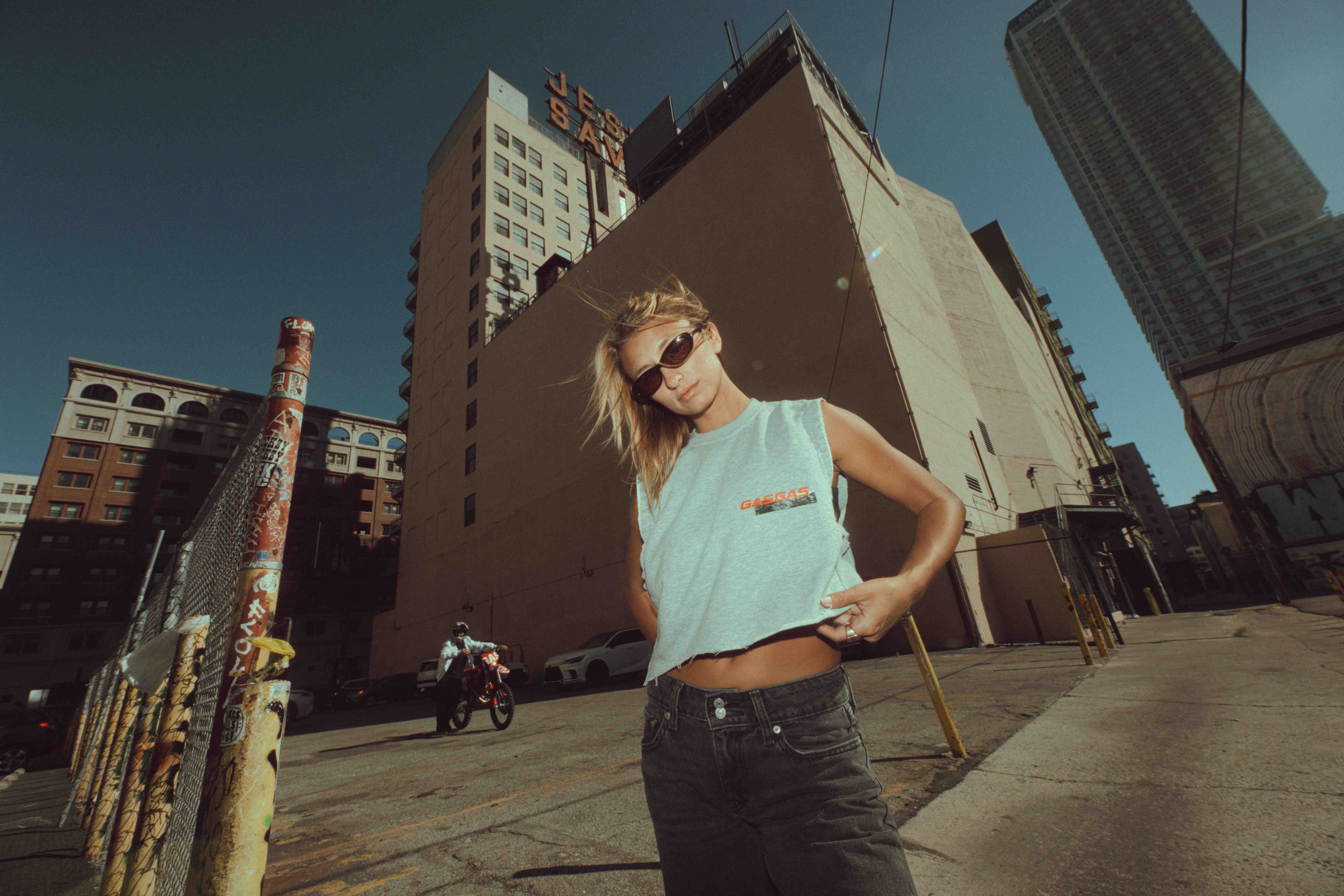 Woman in a turquoise tank top and sunglasses standing in a downtown Los Angeles street