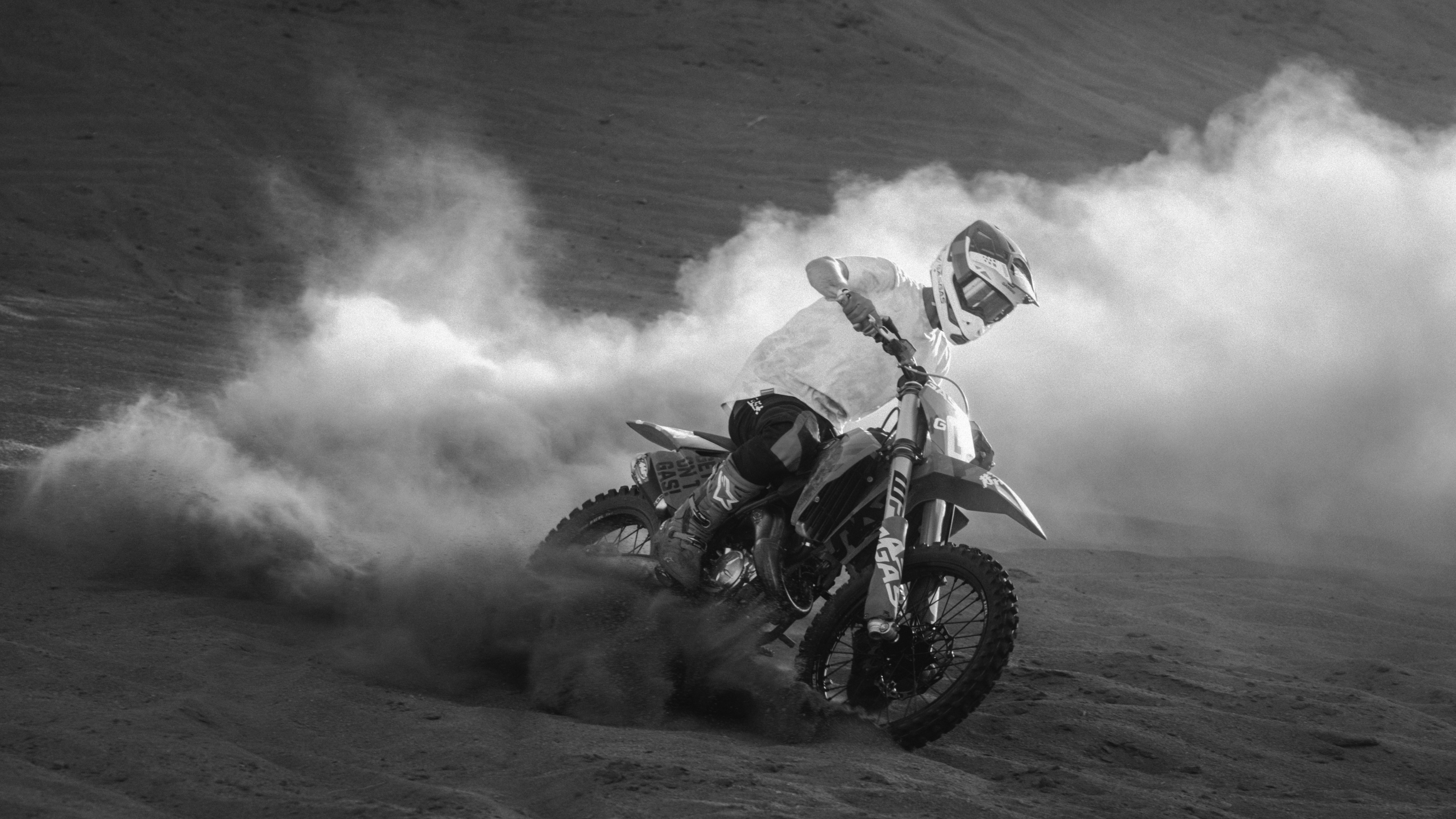 High-contrast black and white GASGAS rider sliding through a cloud of dust