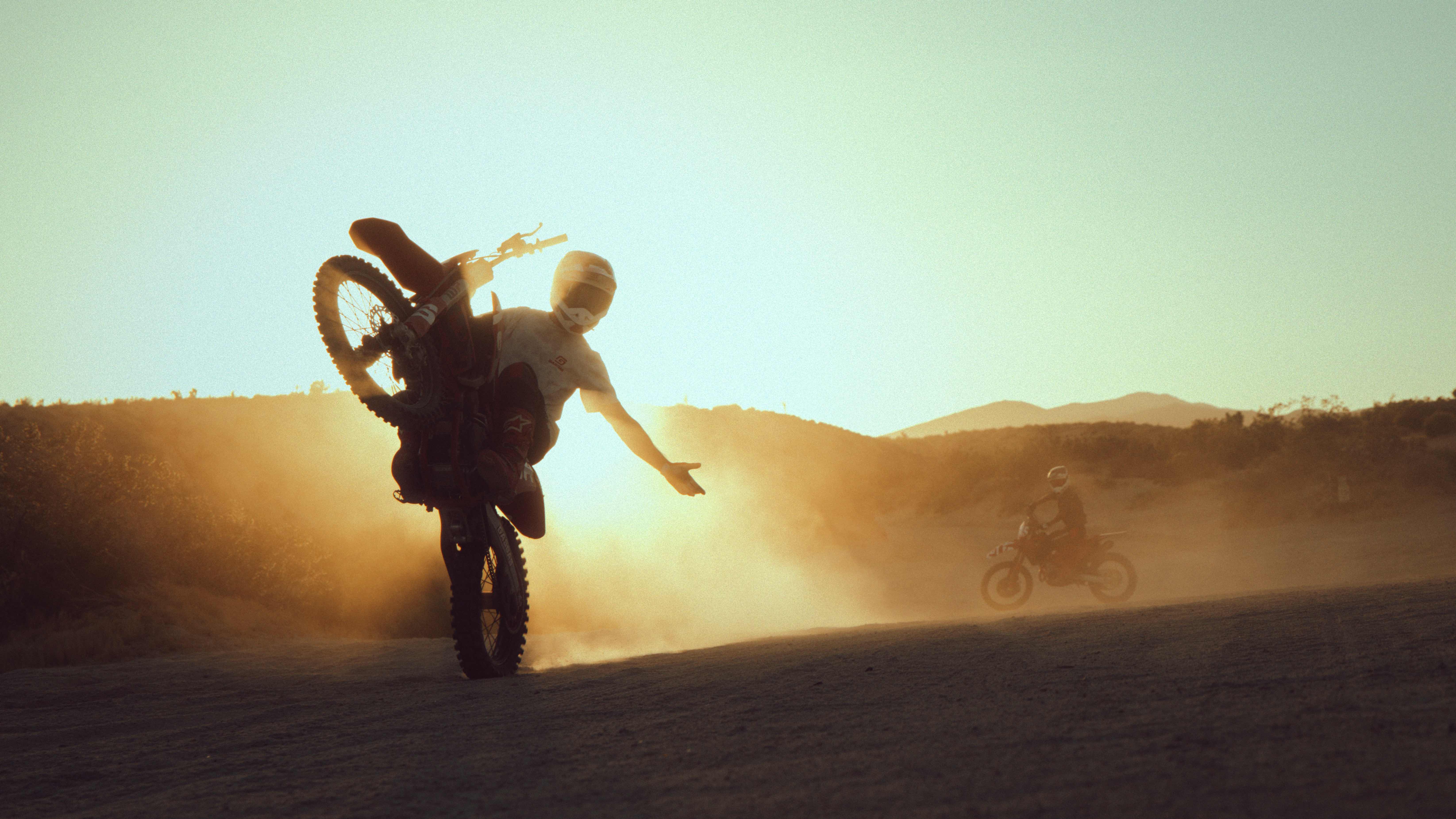 Silhouetted rider pulling a wheelie into backlit sunset dust